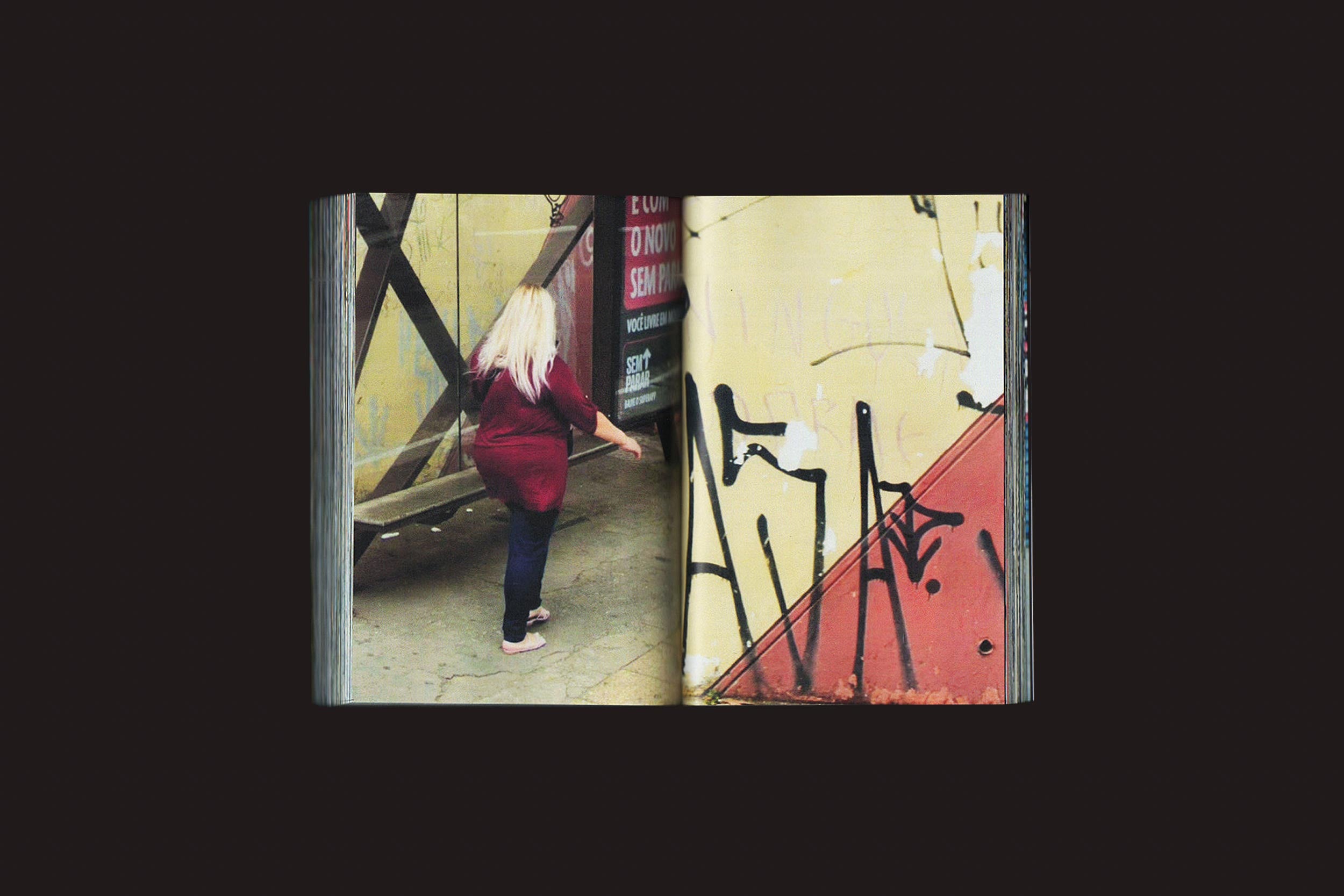 Um livro aberto de fotos Romeu Silva: Passantes, da Zero-Edições, mostra, à esquerda, uma mulher com longos cabelos loiros e camisa vermelha se afastando; à direita, grafite preto em uma parede amarela em São Paulo.