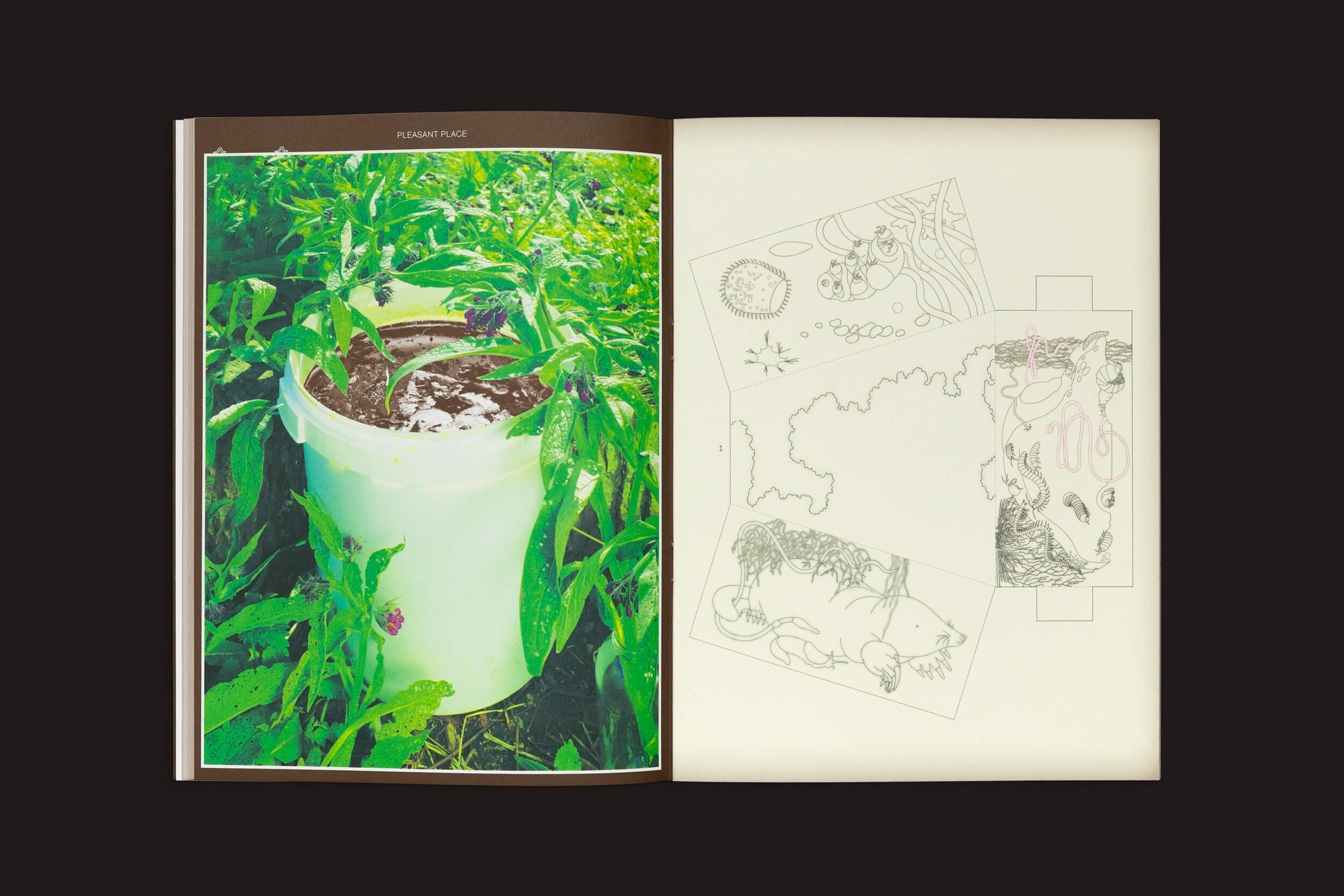Um livro aberto mostra uma foto de um balde branco de Pleasant Place 3: Compost, cercado por plantas verdes na página da esquerda, sugerindo seu propósito de jardinagem. A página da direita apresenta esboços abstratos em preto e branco com formas geométricas e orgânicas.