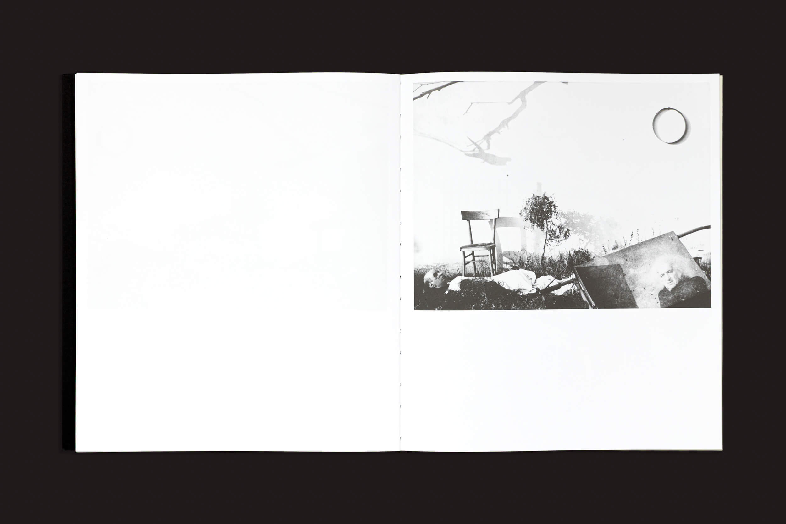 Um livro aberto, "Mario Giacomelli: Questo ricordo lo vorrei raccontare", de Skinnerboox, revela uma foto em preto e branco na página direita representando uma cadeira e uma árvore em meio a pedras e grama, evocando elementos inspiradores. A página esquerda está em branco, com uma borda preta marcante.