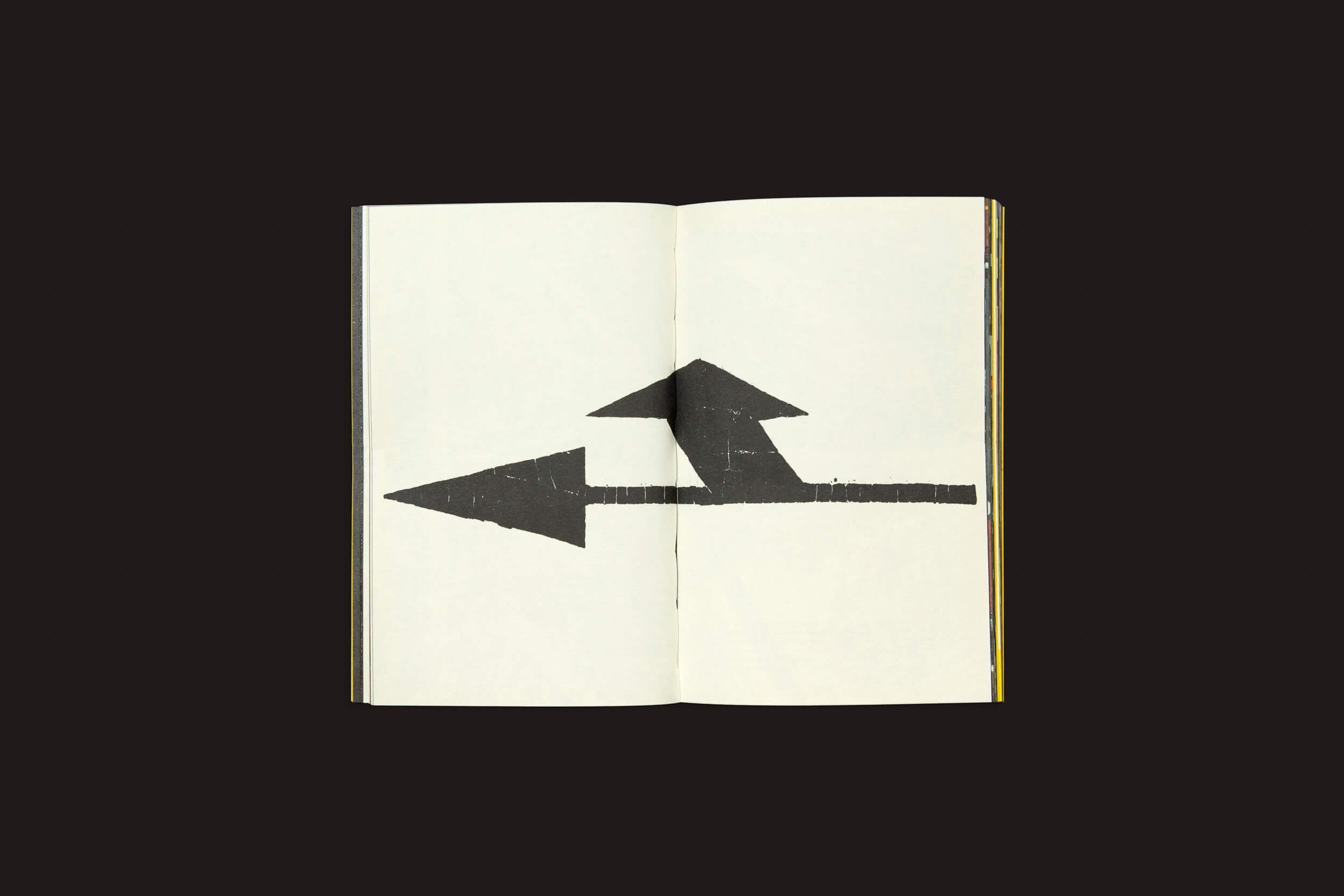 Contra um fundo preto, um livro aberto apresenta uma imagem marcante: uma seta preta ousada apontando para a esquerda, cruzada por outra apontando para cima. Isso captura a essência de Ermãos Monjon: Sinais/Signs da Livros Fantasma, explorando linguagens gráficas semelhantes à deriva urbana.