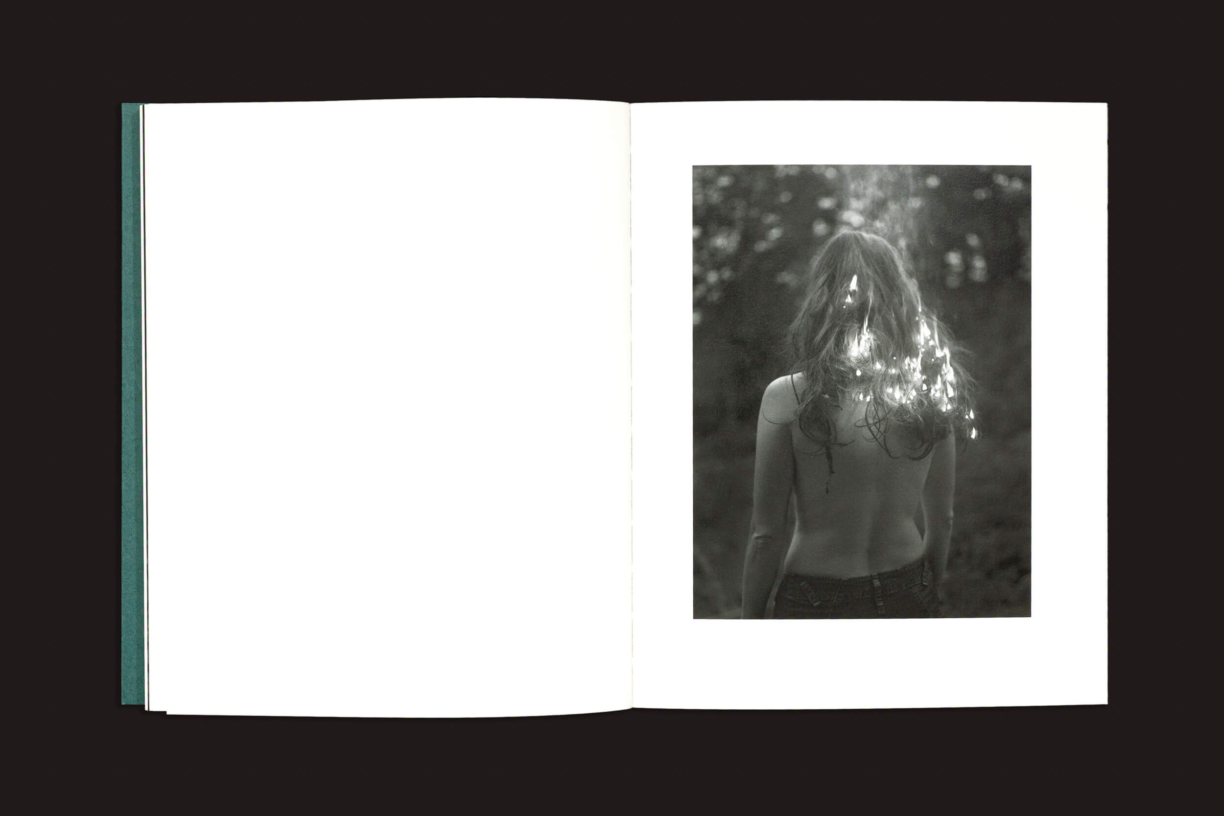 Em "Dylan Hausthor & Pia Paulina Guilmoth: Sleep Creek", de Void, um livro aberto exibe uma foto documental em preto e branco à direita de uma pessoa de topless e cabelos compridos ao ar livre em Peaks Island; a página da esquerda está em branco.