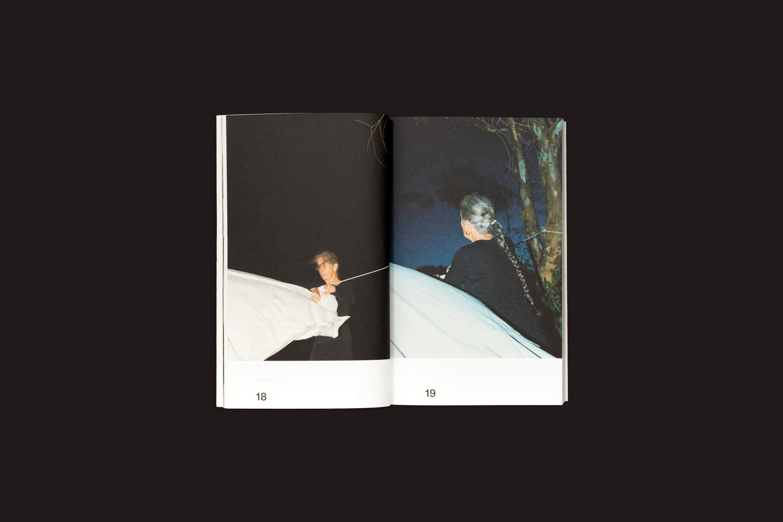 Um livro aberto sobre um fundo escuro mostra imagens de alguém com tecido branco à noite nas páginas 18-19, possivelmente de Some of you Killed Luisa, de Valeria Cherchi, do The Eriskay Connection, sugerindo os misteriosos sequestros na Sardenha entrelaçados com a história evocativa de Luisa.