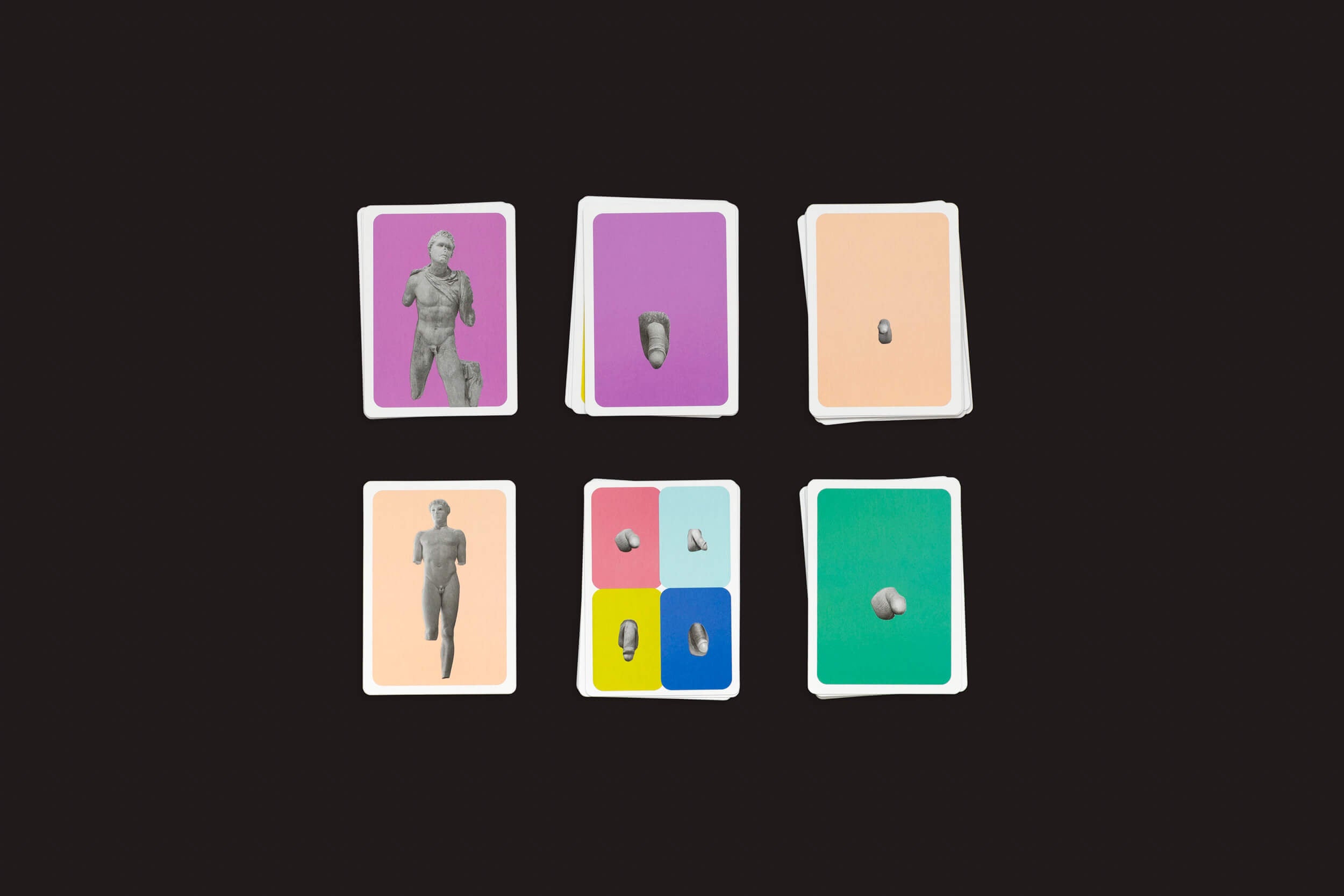 O Jogo do Pênis Grego Perdido da Fraglich Publishing apresenta uma coleção de cartas vibrantes com imagens coloridas: estátuas, rostos e objetos em fundos roxos, brancos e laranja na linha superior; e visuais semelhantes em fundos roxos, azuis, amarelos e verdes na linha inferior.