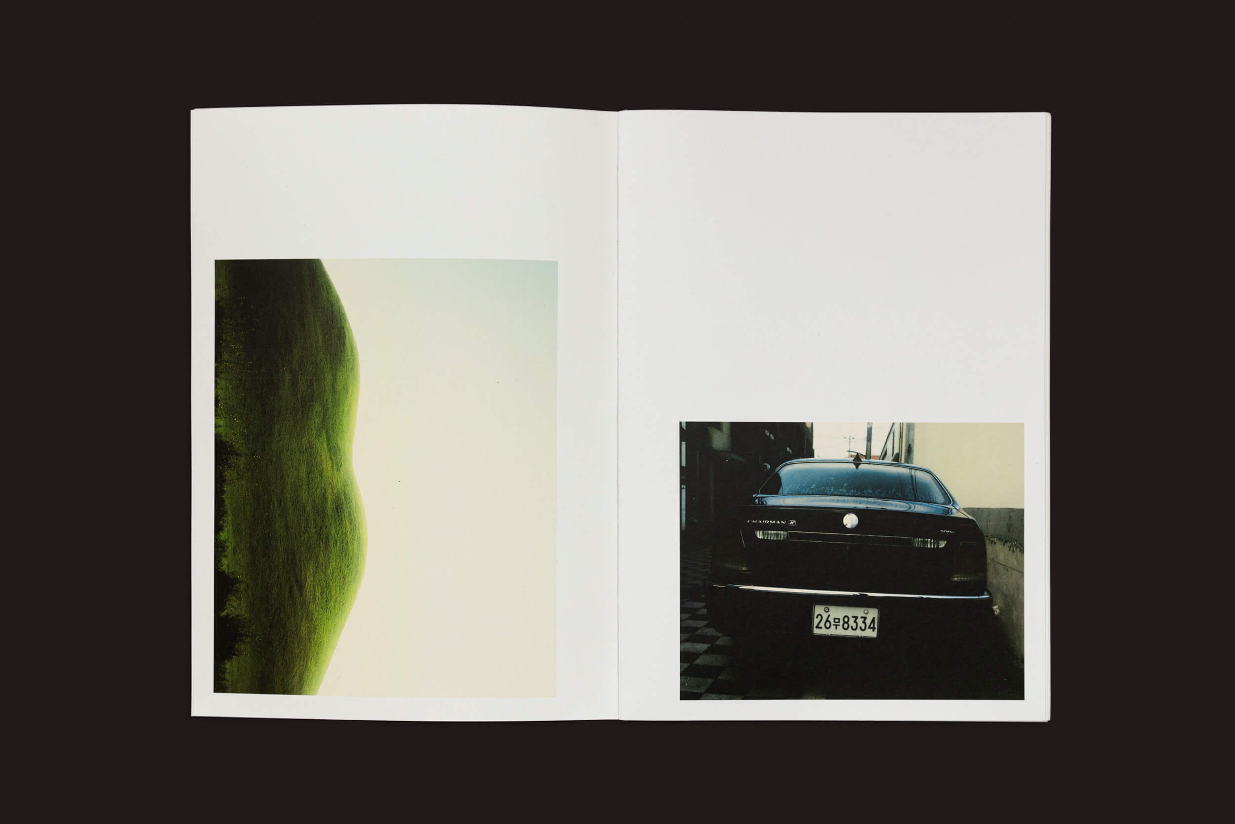 O livro aberto exibe duas páginas: a da esquerda apresenta uma imagem abstrata com uma forma verde e curva em um fundo claro de Eduard Sánchez Ribot: Tierra, Camino, Fruto de Handshake. A da direita mostra uma foto de um carro preto com uma placa estacionado em uma área mal iluminada.