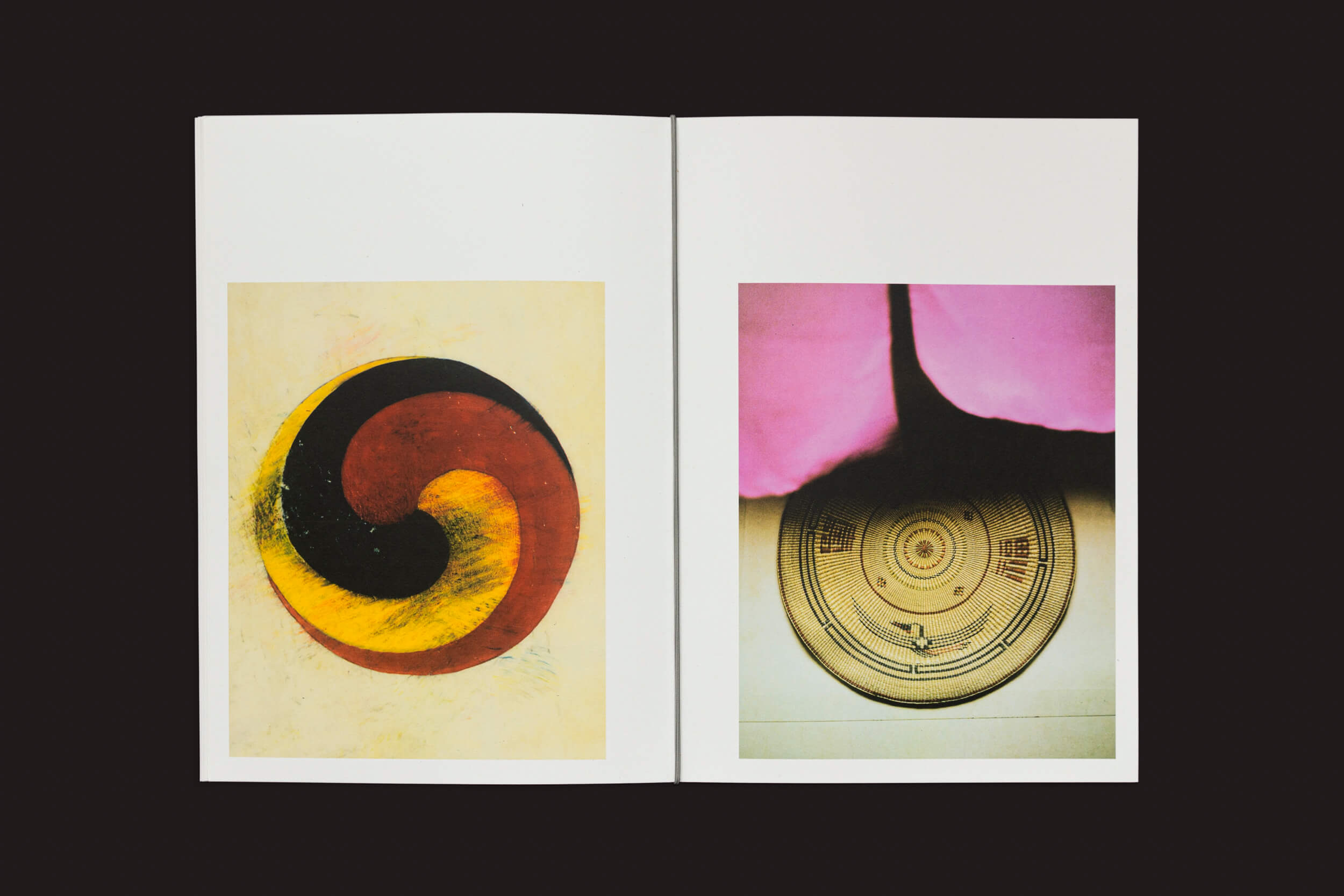 O livro Eduard Sánchez Ribot: Tierra, Camino, Fruto da Handshake mostra duas páginas. A página da esquerda tem um desenho espiral abstrato em vermelho, amarelo e preto que lembra caminhos coloridos. A página da direita mostra um padrão circular sob uma forma rosa; ambas têm bordas brancas.