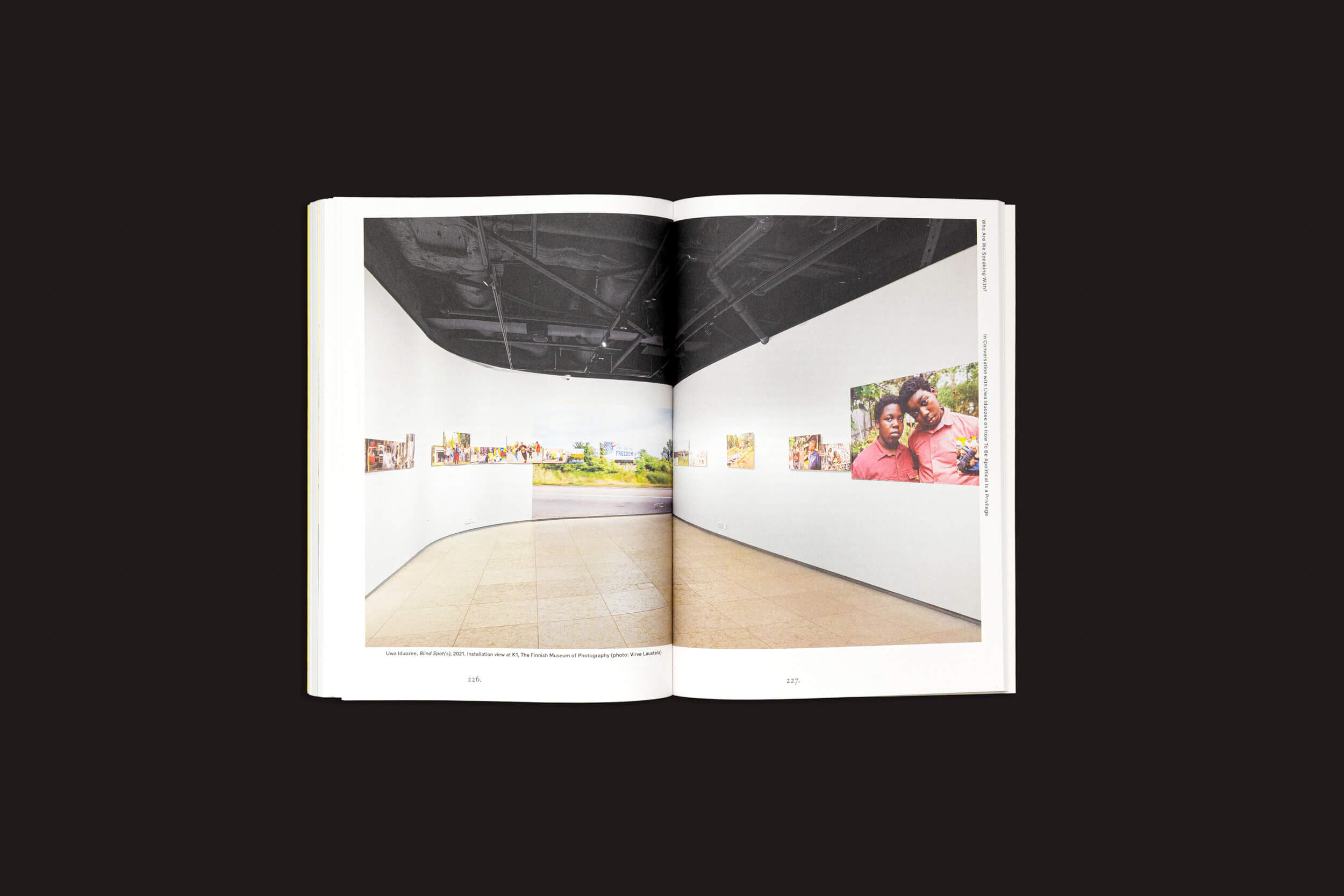 Por que expor? vol. 2 da Fw:Books apresenta uma representação fotográfica impressionante do interior de uma galeria de arte, com obras de arte vibrantes em paredes brancas, teto preto e piso de cerâmica marrom claro, tudo contrastando de forma impressionante com o fundo preto simples.