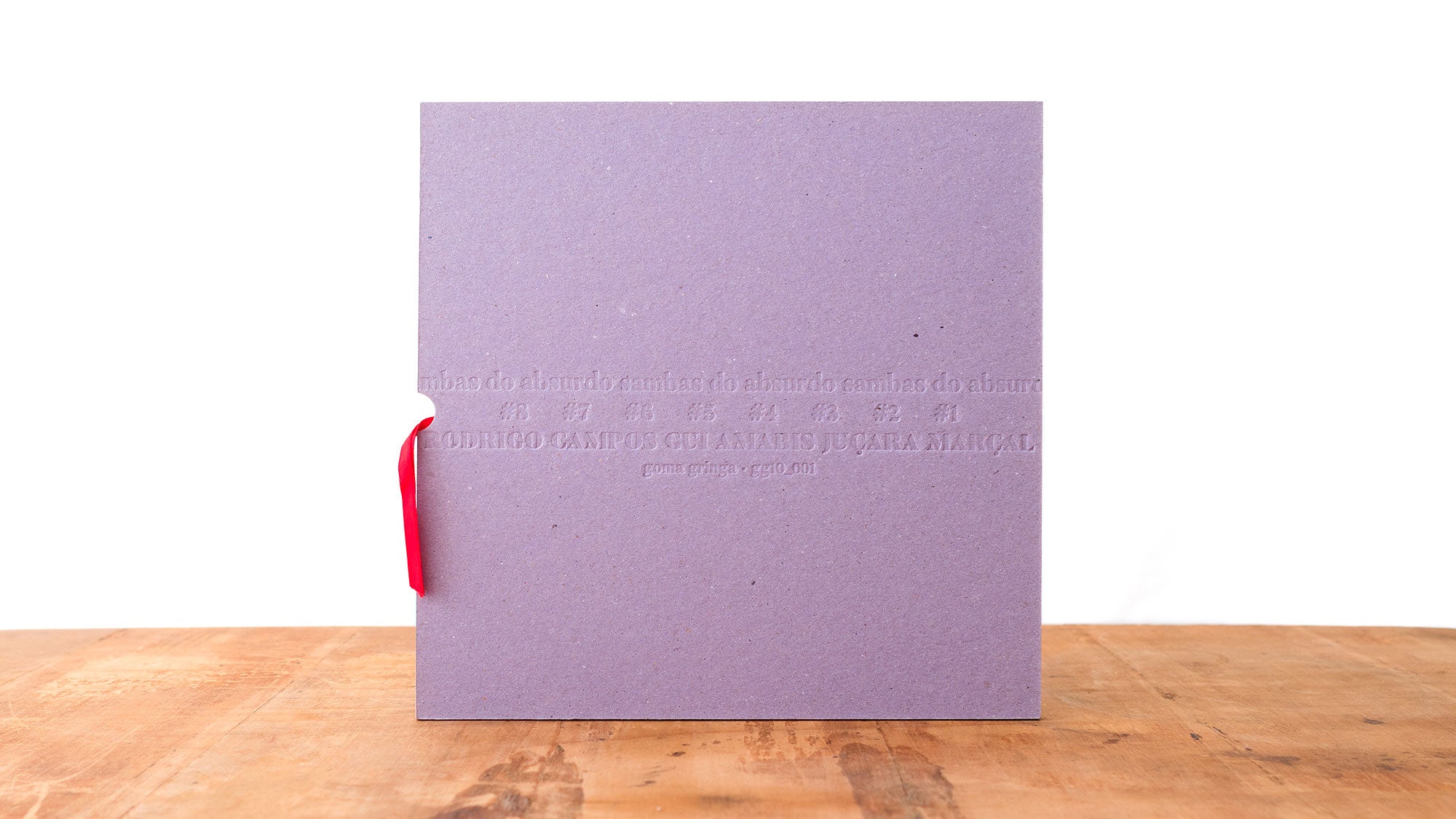 Uma pasta quadrada, texturizada em roxo, com texto em relevo e uma fita vermelha está em pé sobre uma superfície de madeira, contra um fundo branco liso.