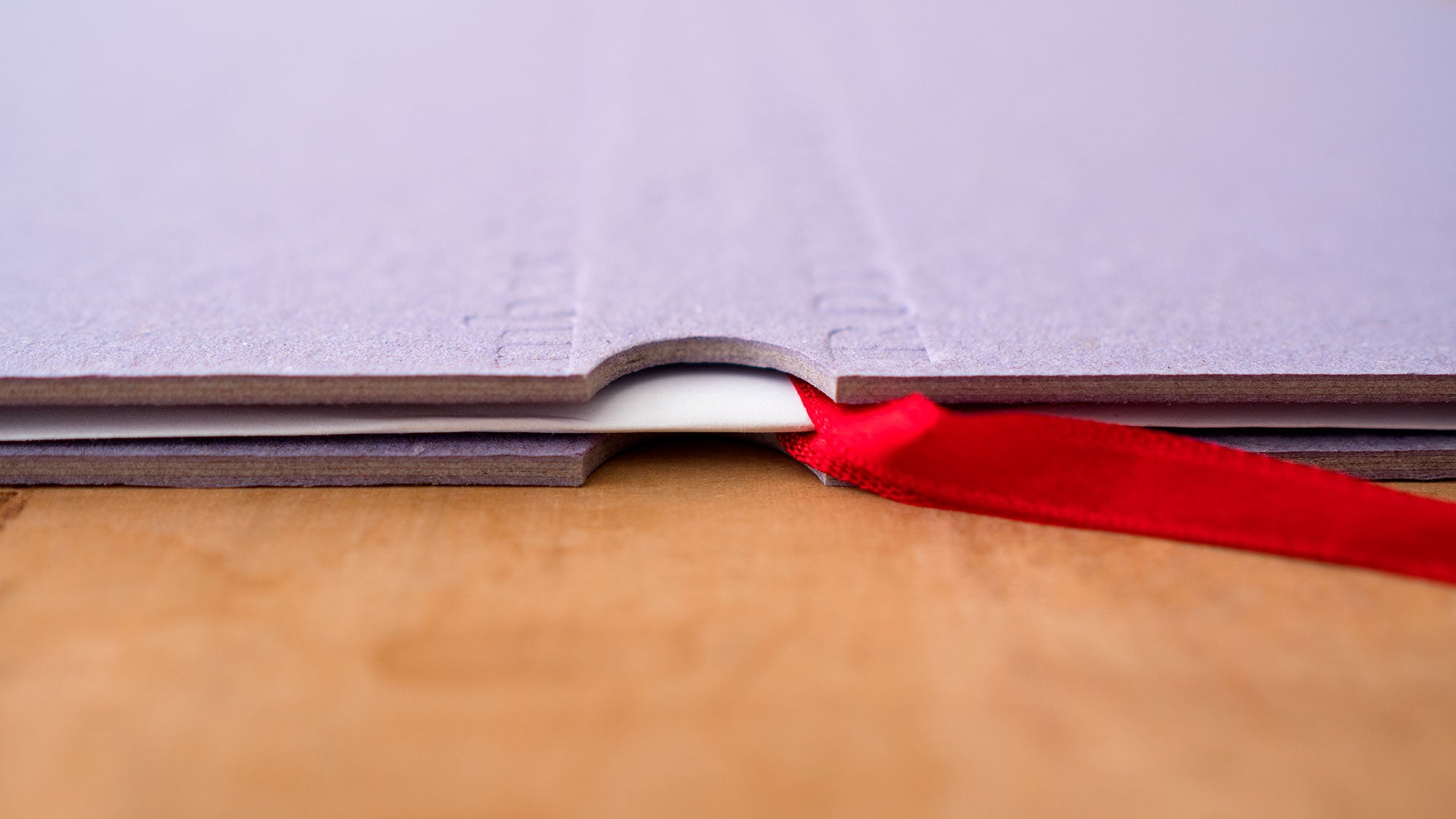 Close-up de um livro com capa roxa aberto sobre uma superfície de madeira, mostrando um marcador de fita vermelha entre as páginas.