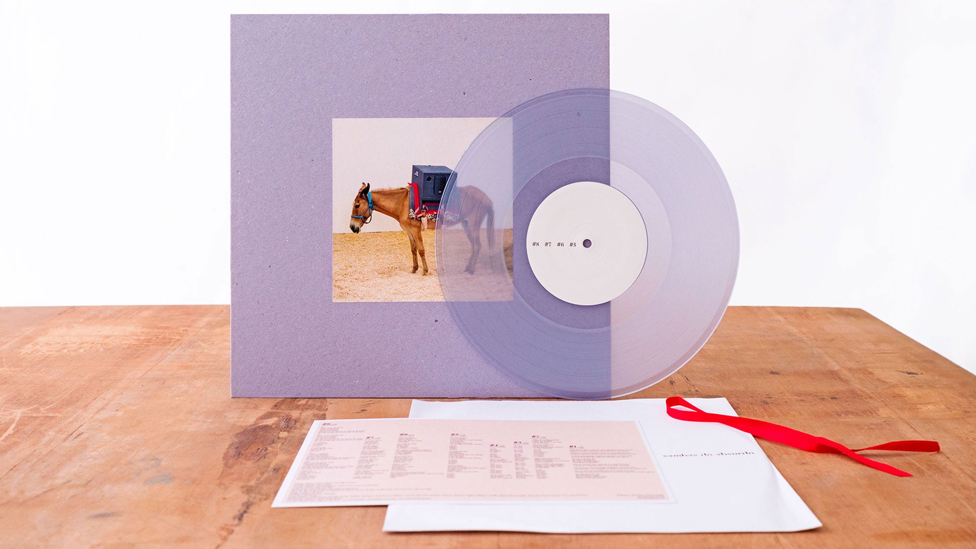 Um disco de vinil roxo translúcido cobre parcialmente a capa do álbum, que apresenta um cavalo usando uma máscara semelhante a uma caixa. O disco, uma folha com a letra da música e um envelope com uma fita vermelha repousam sobre uma mesa de madeira.