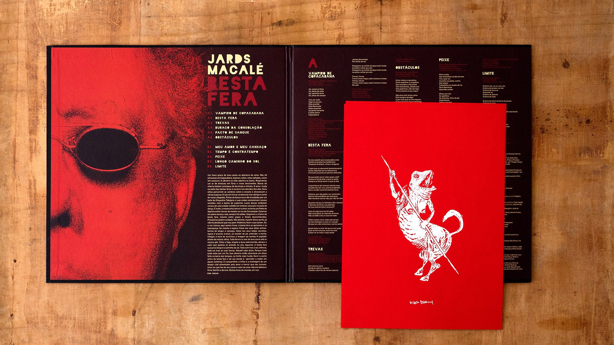 Um livreto aberto com um design vermelho e preto, apresentando um rosto parcial com óculos de sol na página esquerda e texto na direita. Uma capa vermelha com uma ilustração branca de um rato segurando uma lança está colocada no topo.