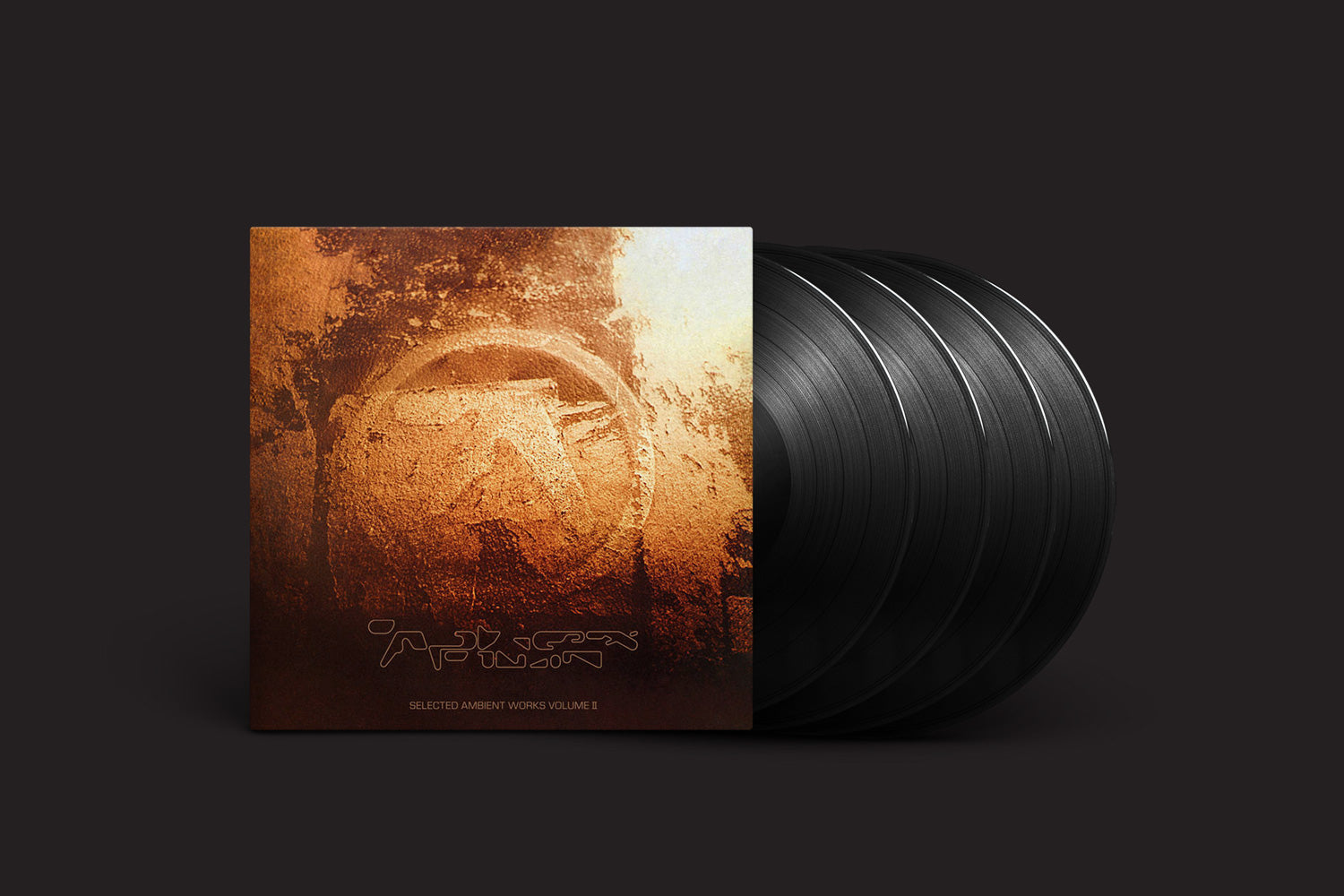 O box set de vinil "Aphex Twin: Selected Ambient Works Volume II (Expanded Edition)" da Warp traz cinco discos pretos e uma capa inspirada no original. Ele ostenta um design abstrato terroso com tons de marrom e dourado, um emblema circular desgastado no centro, texto estilizado abaixo e um fundo escuro.