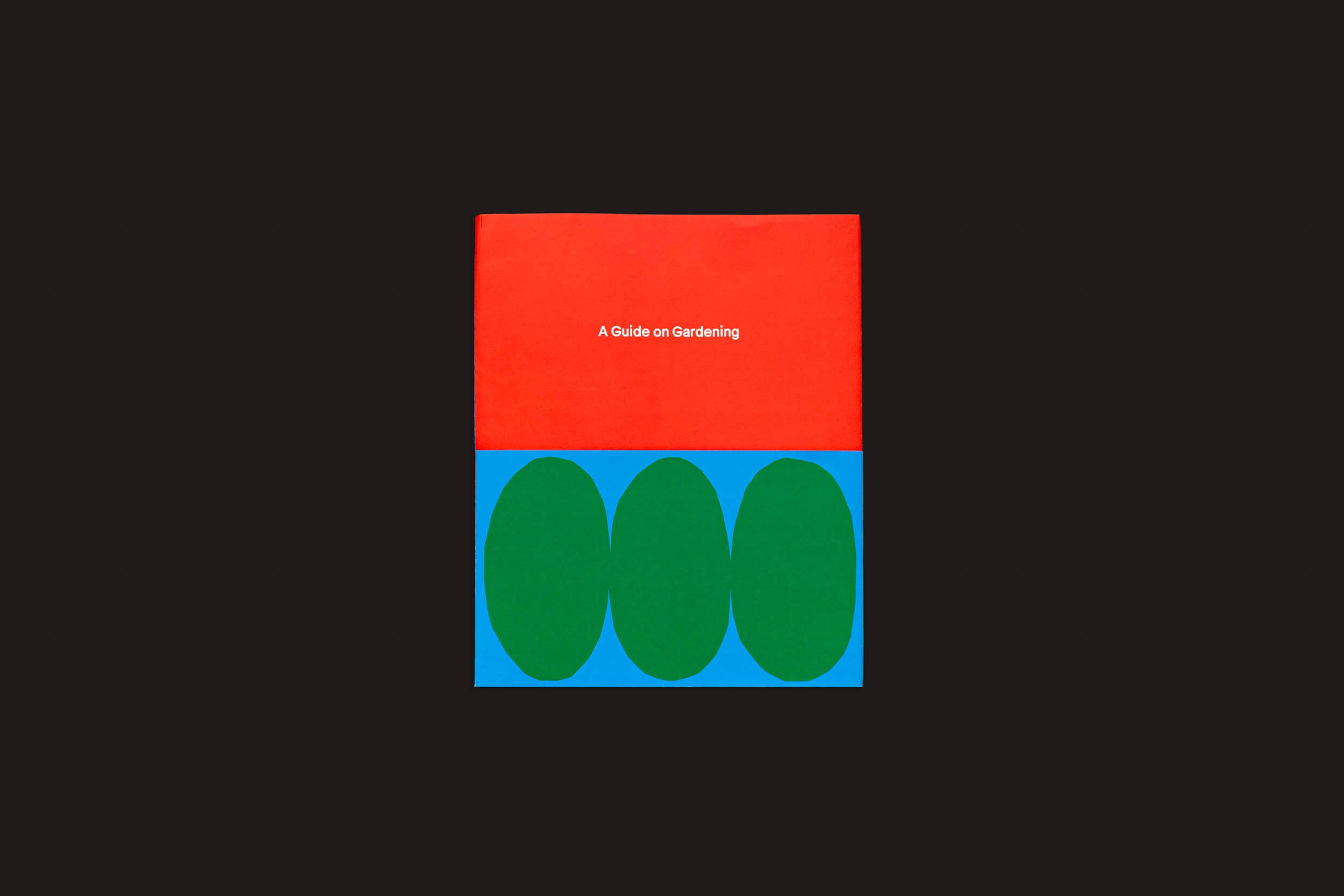 A imagem mostra uma capa minimalista para Rubén Montesinos: A Guide on Gardening da Handshake. A metade superior é vermelha com o título branco, e a metade inferior é azul com três ovais verdes simbolizando expressões vibrantes de topiário cultural, tudo em um fundo preto.