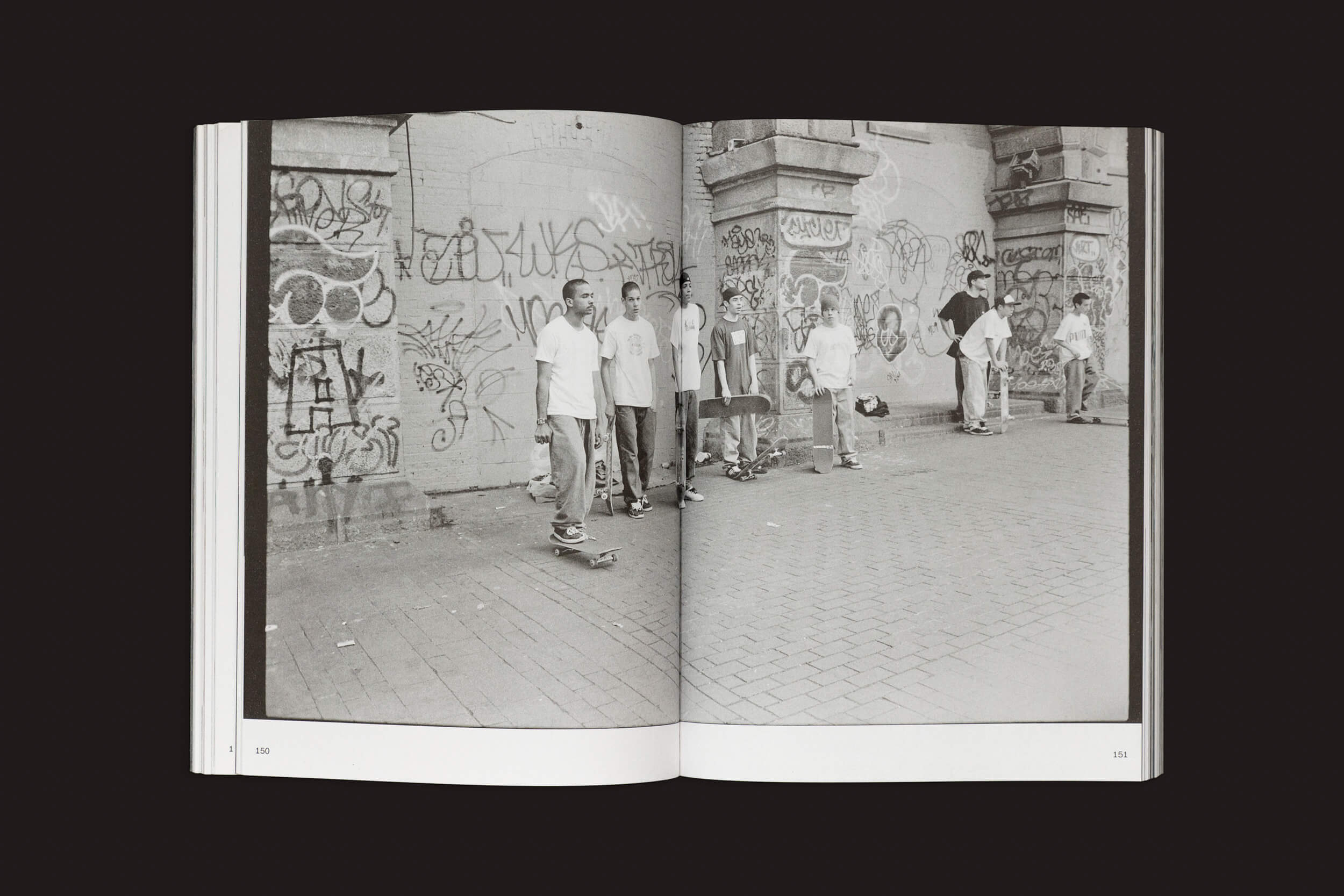 Uma foto em preto e branco de Ari Marcopoulos: Beware da Roma Publications retrata pessoas perto de uma parede coberta de grafite, algumas com skates. Evocando a cultura urbana, ela é apresentada em um livro aberto da coleção do Musée dArt Moderne de Paris.