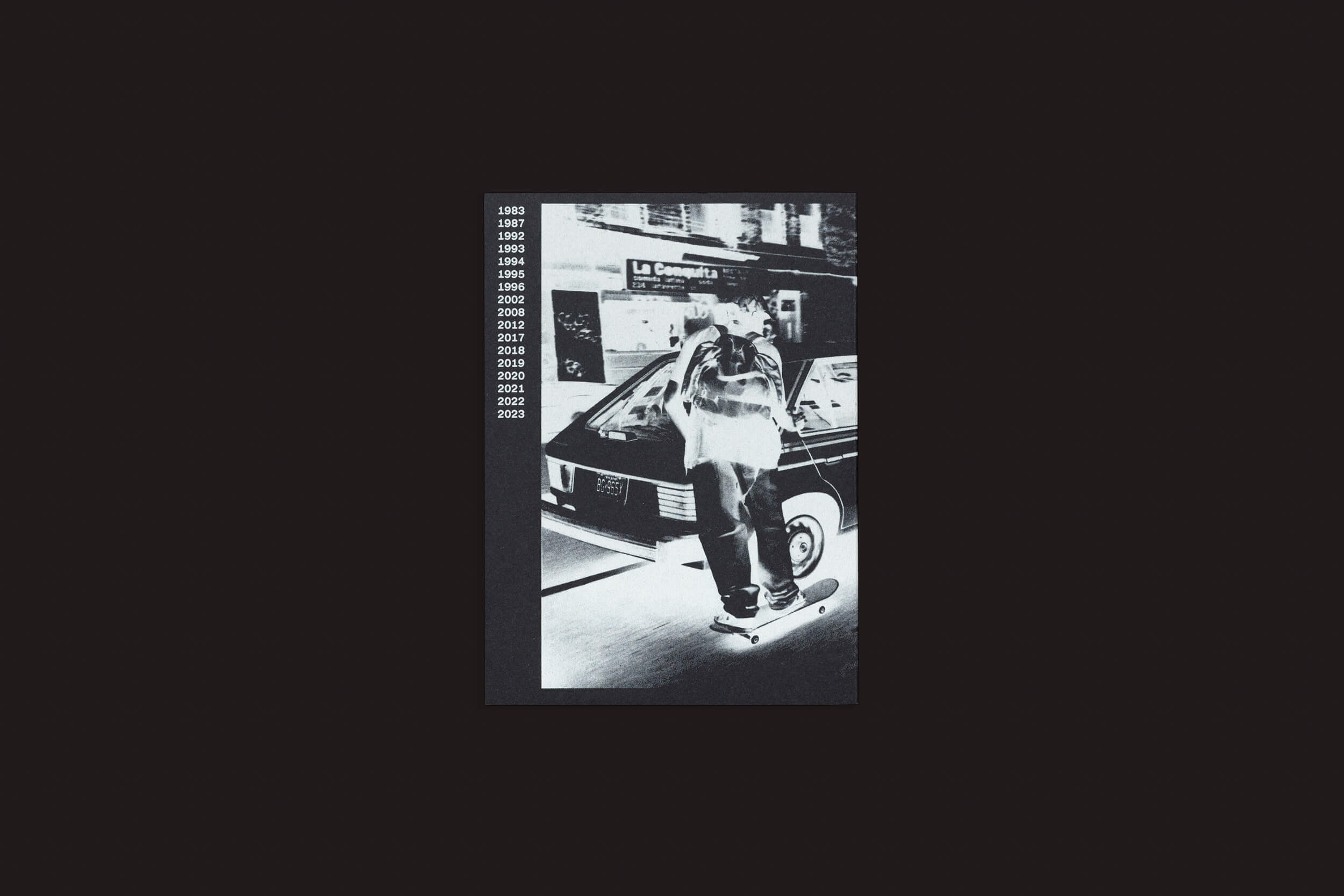 A impressionante imagem em preto e branco evoca o estilo de Ari Marcopoulos de Ari Marcopoulos: Beware da Roma Publications, retratando um skatista em uma rua com um carro atrás. Uma linha do tempo vertical de 1989 a 2023 corre ao longo da esquerda, e La Consigne é visível à distância.