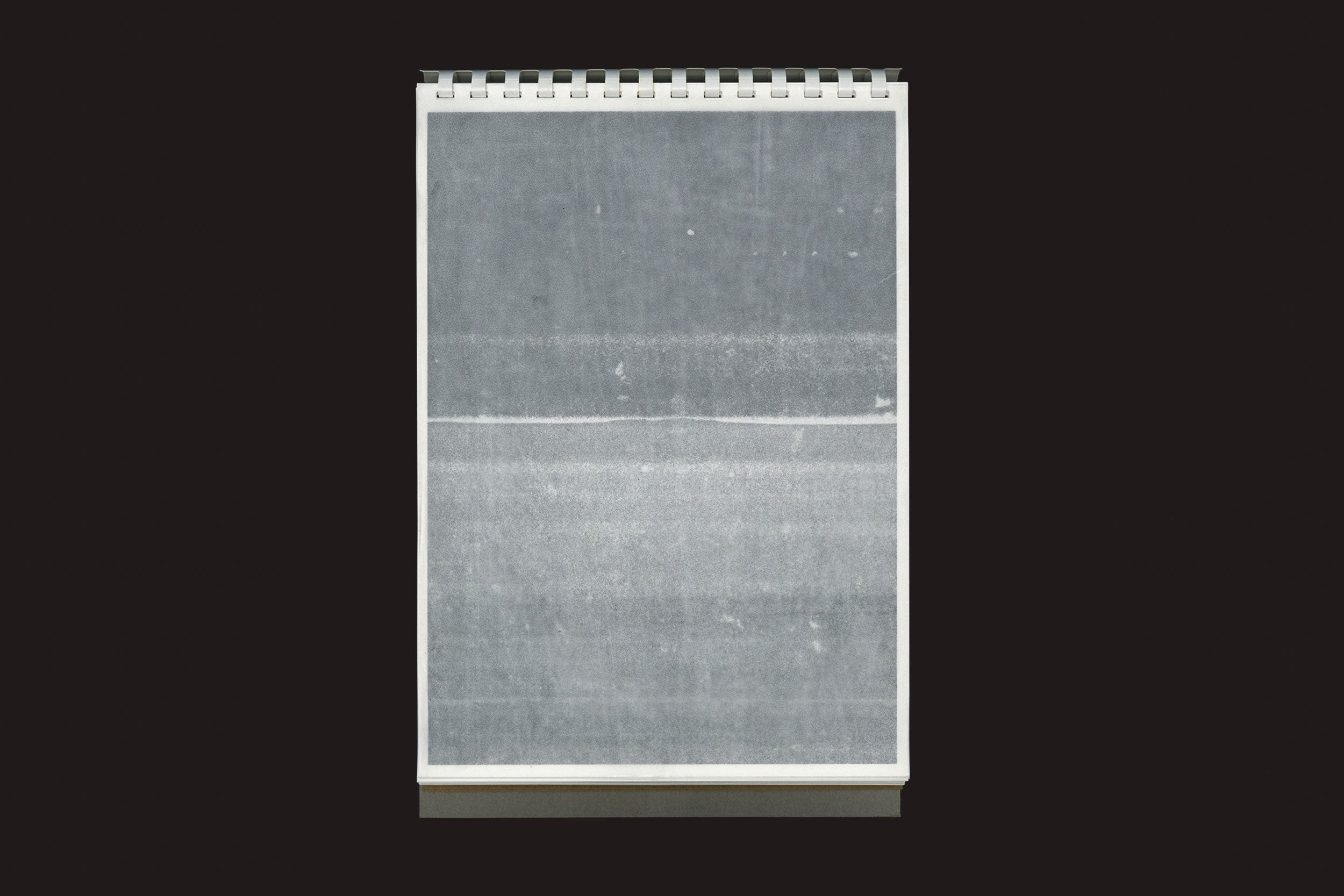 O bloco de notas Hong Shu-ying: 尘惦 (chéndiàn) - after scans and lingering dust da Temporary Press está na vertical, com uma página em branco e acinzentada contra um fundo preto, semelhante a uma fotocópia de partituras, sem texto ou desenhos visíveis.