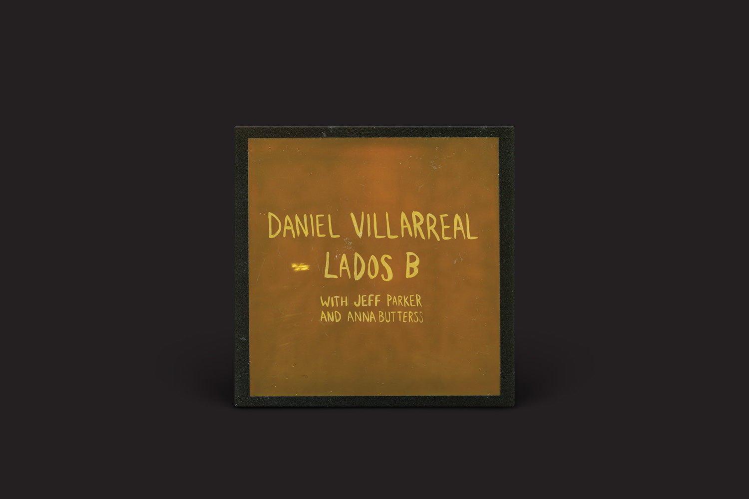A capa do álbum tem um fundo escuro com texto amarelo vibrante: "Daniel Villarreal: Lados B", com Jeff Parker e Anna Butterss, da International Anthem Recording Company.