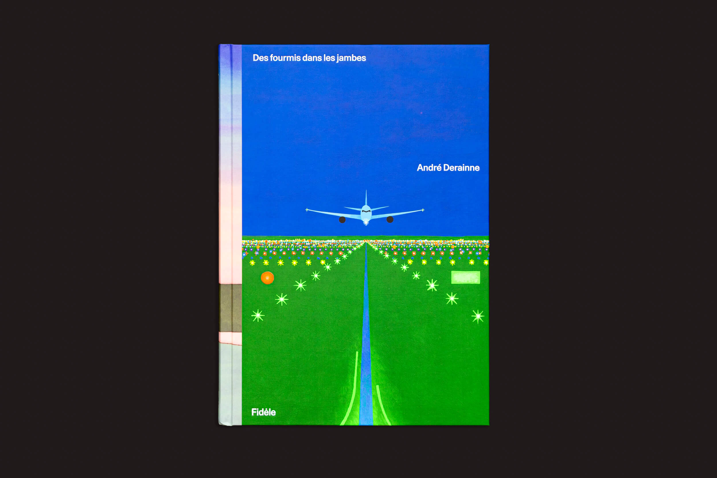 André Derainne: Des fourmis dans les jambes da Fidéle Editions apresenta uma capa estilizada que mostra um avião pousando em uma pista iluminada sob um céu azul escuro.