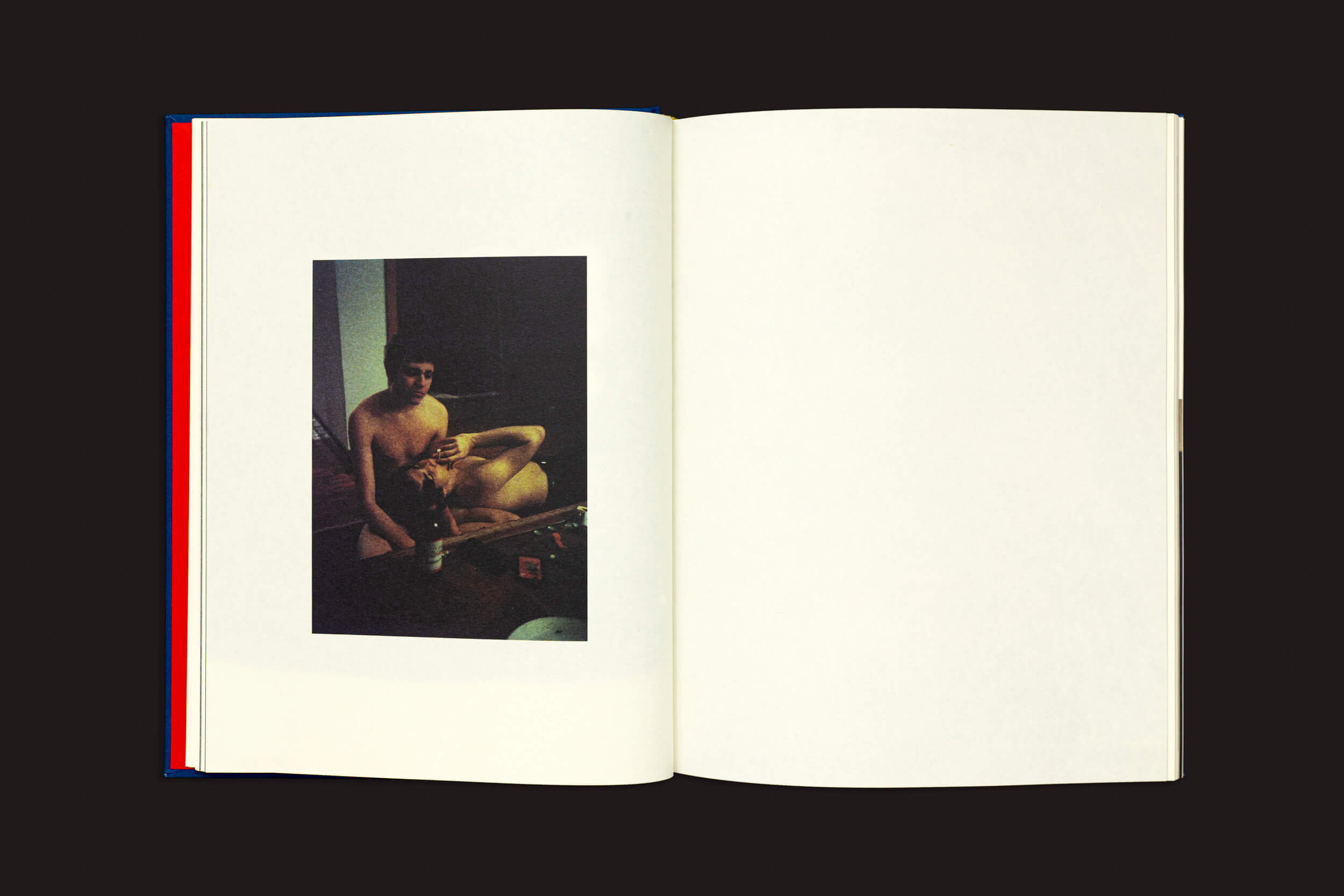 Em "Igor Morales: Em um Tritão me transformarei eventualmente", da Editora Madalena, um livro aberto exibe uma pequena foto escura de uma figura nua em um ambiente interno à esquerda, evocando emoções e incertezas; a página direita está em branco, sobre fundo preto.
