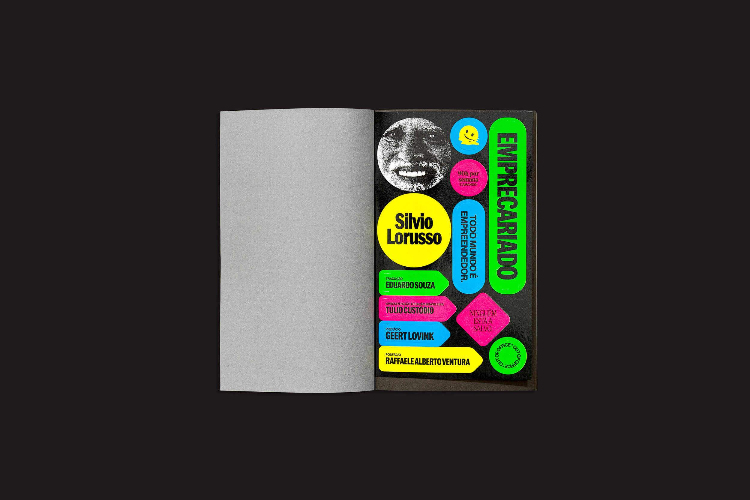 O livro aberto exibe uma página com adesivos vibrantes em um fundo preto, incluindo "Silvio Lorusso" e "EMPRECARADO". Essas expressões coloridas em verde, rosa, azul e amarelo celebram a cultura emprecariado. Produto: Silvio Lorusso: Emprecariado do Clube do Livro do Design.