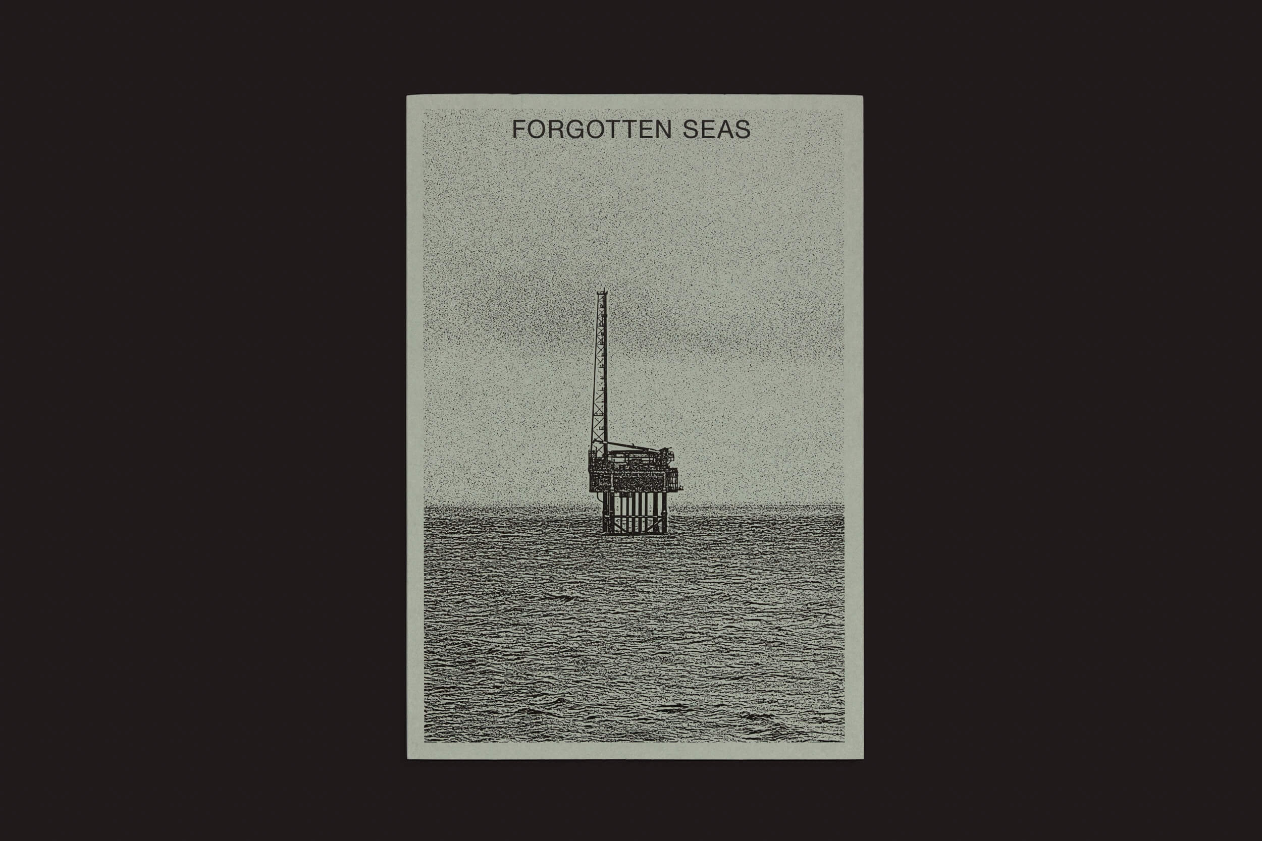 Uma imagem em tons de cinza de uma plataforma de petróleo offshore no mar com Tanja Engelberts: Forgotten Seas acima. Esta plataforma isolada, central para a indústria de petróleo e gás, fica sozinha contra um horizonte árido sob um céu escuro. Produto por The Eriskay Connection.