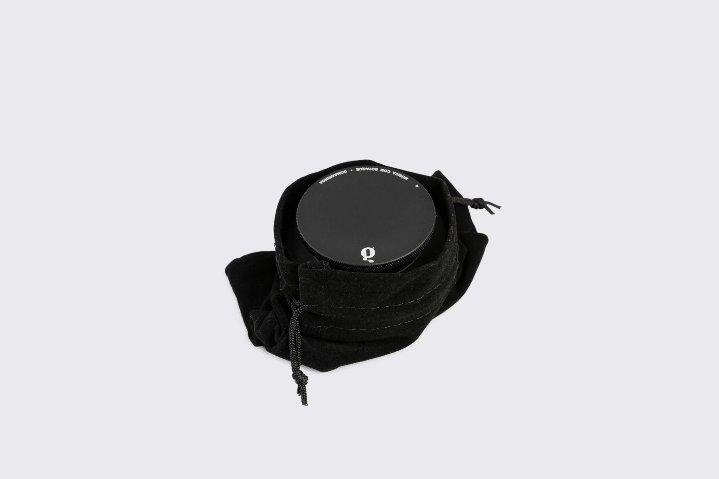 Um objeto preto redondo, o Estabilizador de Disco: Modelo A da Goma Gringa, envolto em tecido preto macio com cordões, repousa elegantemente sobre um fundo branco simples.