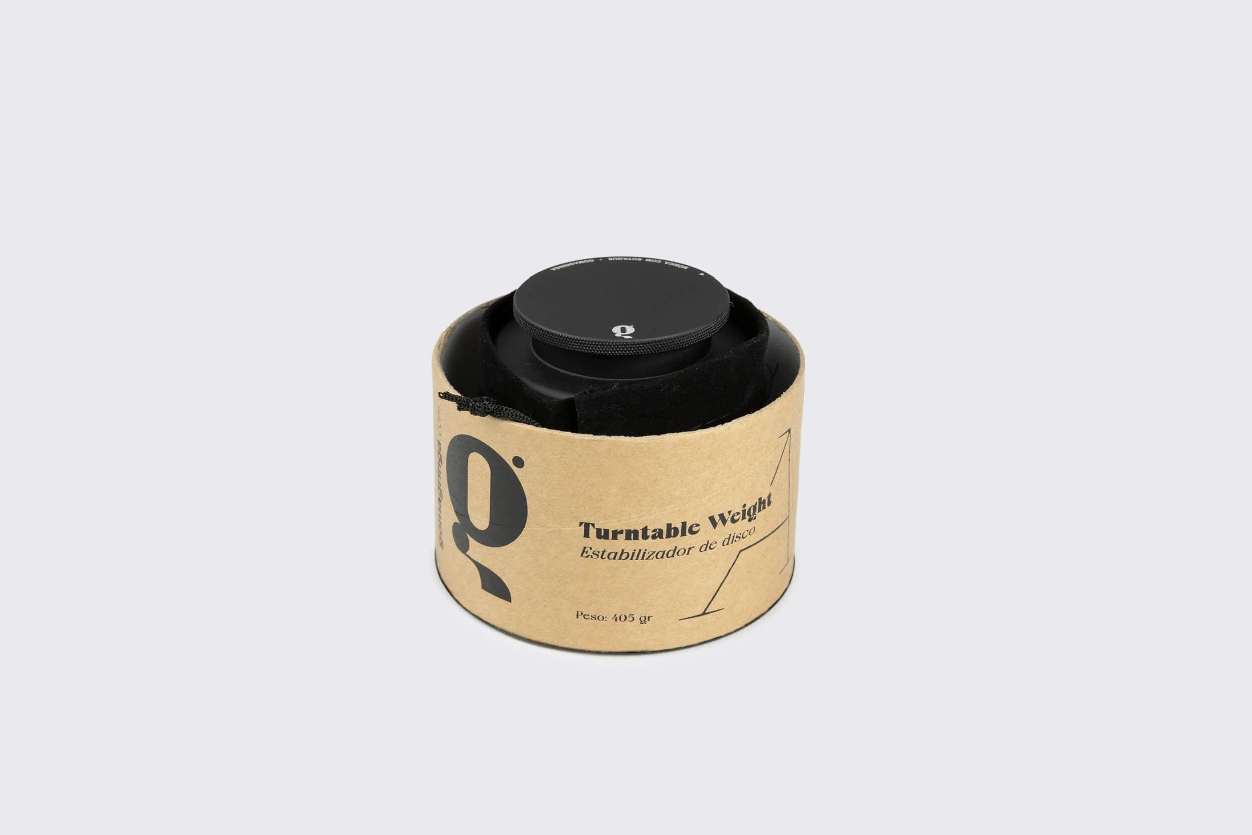 O Goma Gringa Estabilizador de Disco: Modelo A é um peso giratório de alumínio anodizado preto (Peso: 605 g), envolto em embalagem cilíndrica de papelão rotulada "Turntable Weight". Esta peça de edição limitada contrasta com o fundo cinza claro simples.