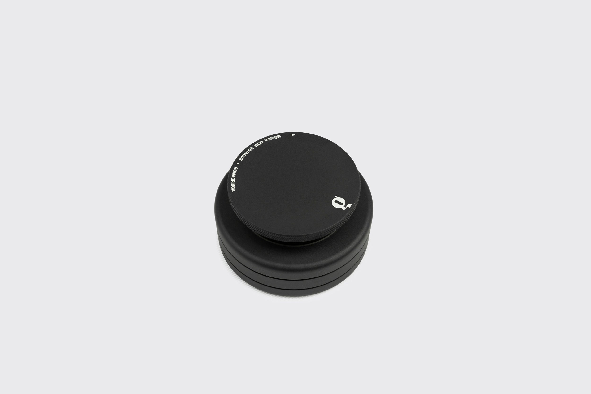 Um peso de toca-discos preto, redondo e empilhável, feito de alumínio anodizado com tampa texturizada, texto branco mínimo e logotipo pequeno, mostrado em um fundo cinza claro simples.