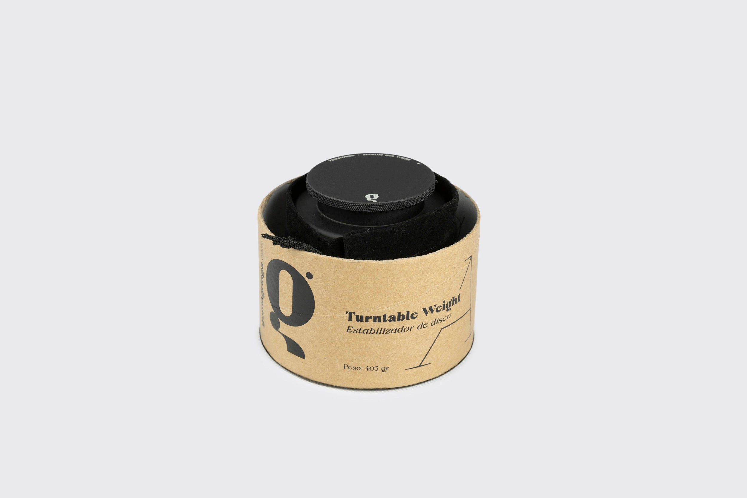 Um Estabilizador de Disco: Modelo A de alumínio preto anodizado da Goma Gringa, pesando 605g, fica em um suporte cilíndrico de papelão rotulado “Turnttable Weight” e “Estabilizador de disco” sobre um fundo cinza claro.