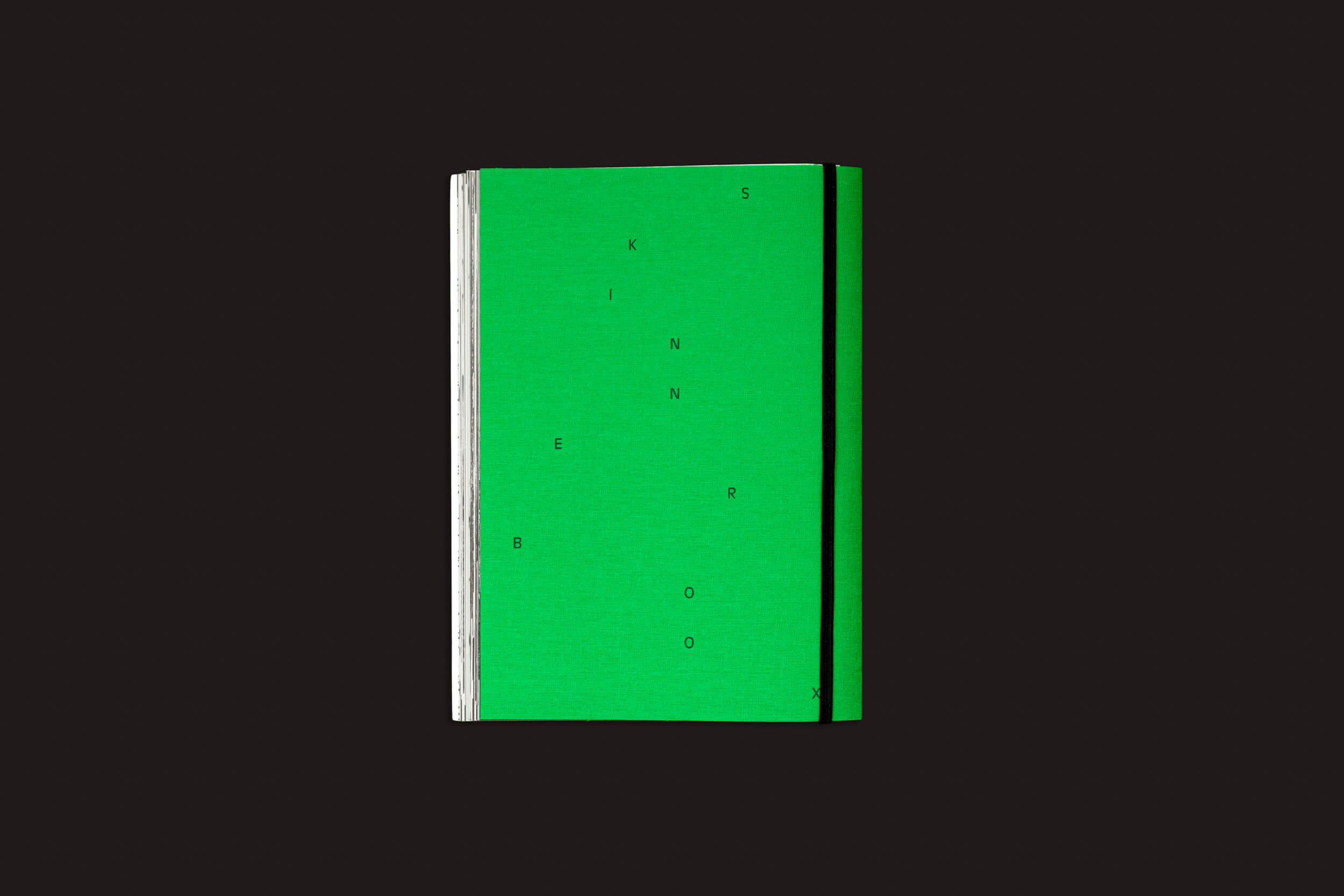Um livro fechado, de capa dura verde, com lombada branca — Index Naturae: Vários Artistas, de Skinnerboox — está centralizado sobre um fundo preto. Letras pretas dispersas estão impressas na frente, evocando os enigmáticos livros fotográficos. Sem título ou autor visíveis.