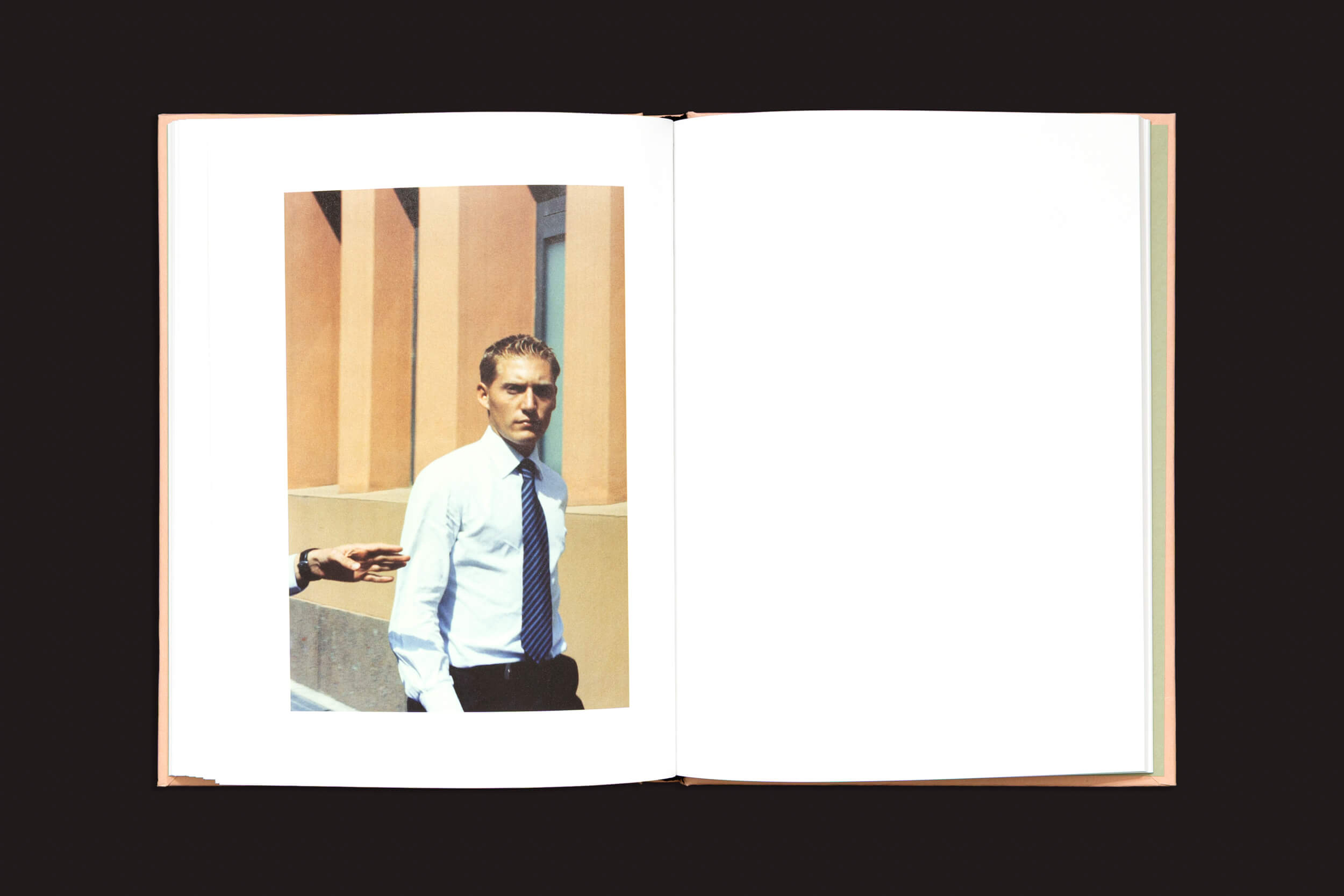 Um livro aberto intitulado "Federico Clavarino: Italia O Italia", de Void, repousa sobre uma superfície escura, exibindo a foto de um homem de camisa branca e gravata, perto de um prédio. Uma mão aparece gesticulando em sua direção, capturando o estilo fotográfico simbólico de Clavarino.