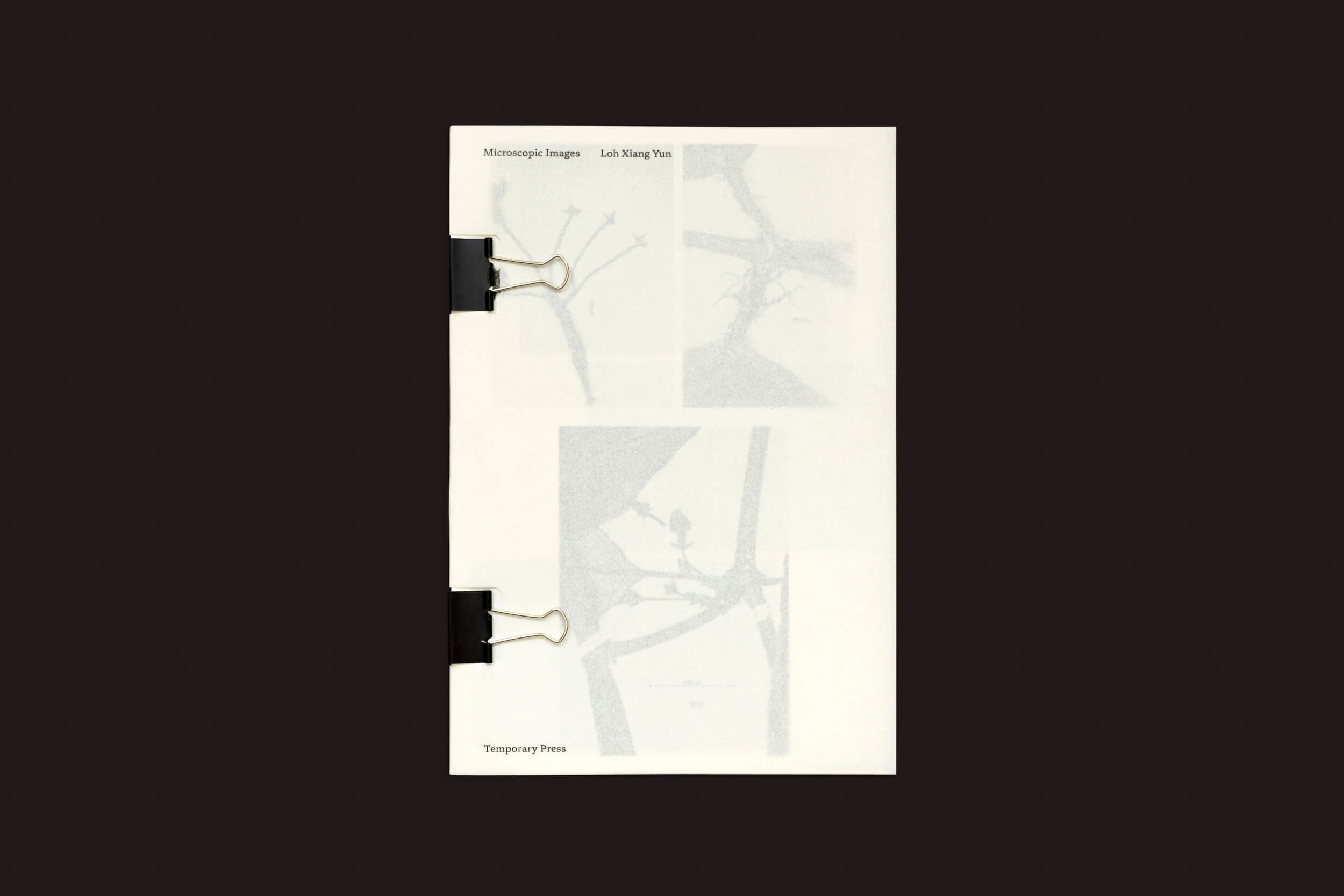 Um livreto intitulado Microscopic Images de Loh Xiang Yun, publicado pela Temporary Press, é recortado com clipes de fichário pretos. A capa mostra imagens em tons de cinza tênues de estruturas microscópicas.