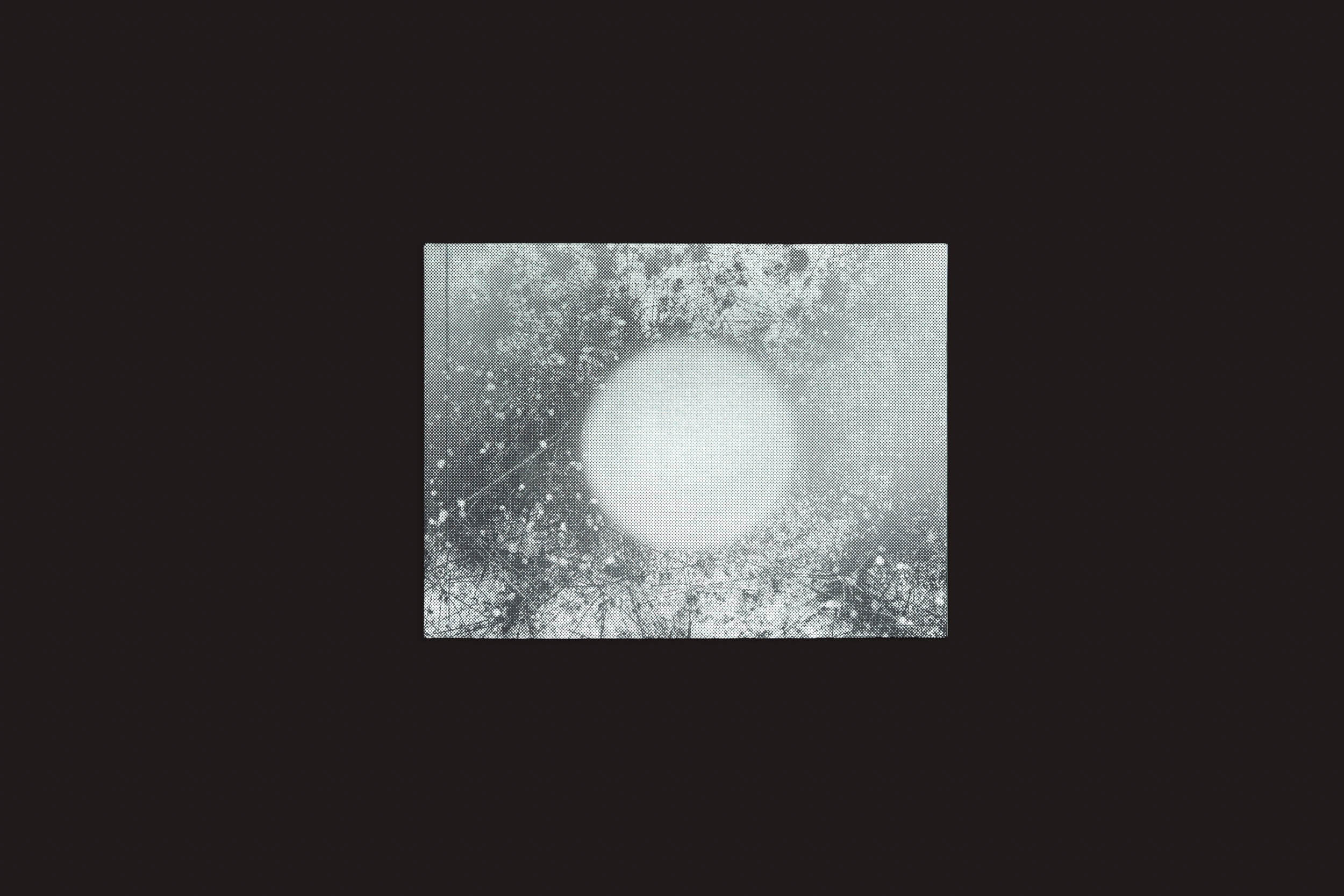 Uma imagem retangular de Bárbara Lissa & Maria Vaz: Óris de Selo Turvo apresenta uma luz branca circular e brilhante em seu centro, cercada por padrões cinzas nebulosos como geada abstrata. O fundo preto destaca a luz central, evocando imagens-paisagens da era Antropoceno.