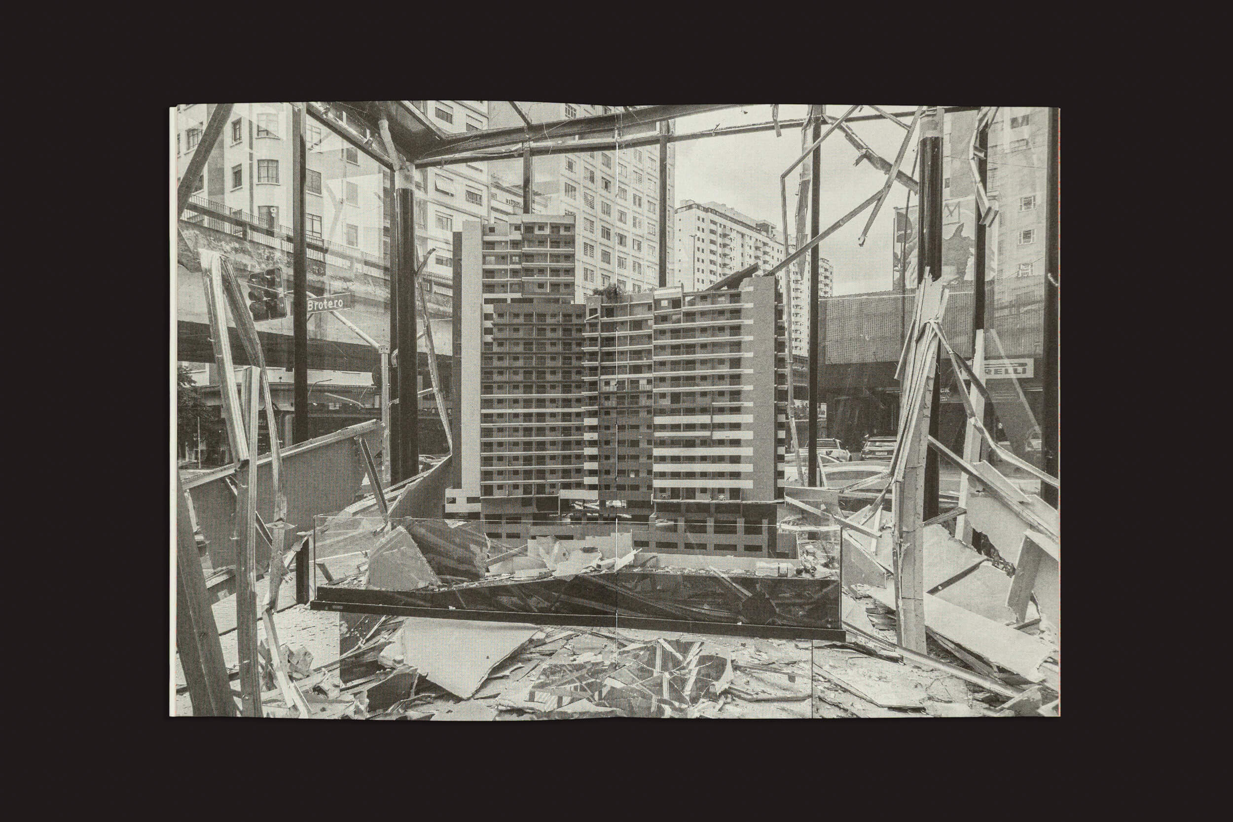 Uma vitrine de vidro estilhaçado exibe uma maquete de um arranha-céu, cercado por escombros. Prédios altos ao fundo personificam o caos arquitetado, pintando um quadro vívido de decadência urbana ou destruição em meio a um deserto de máquinas — capturado em Gui Marcondes: Ossada, de Selo Turvo.
