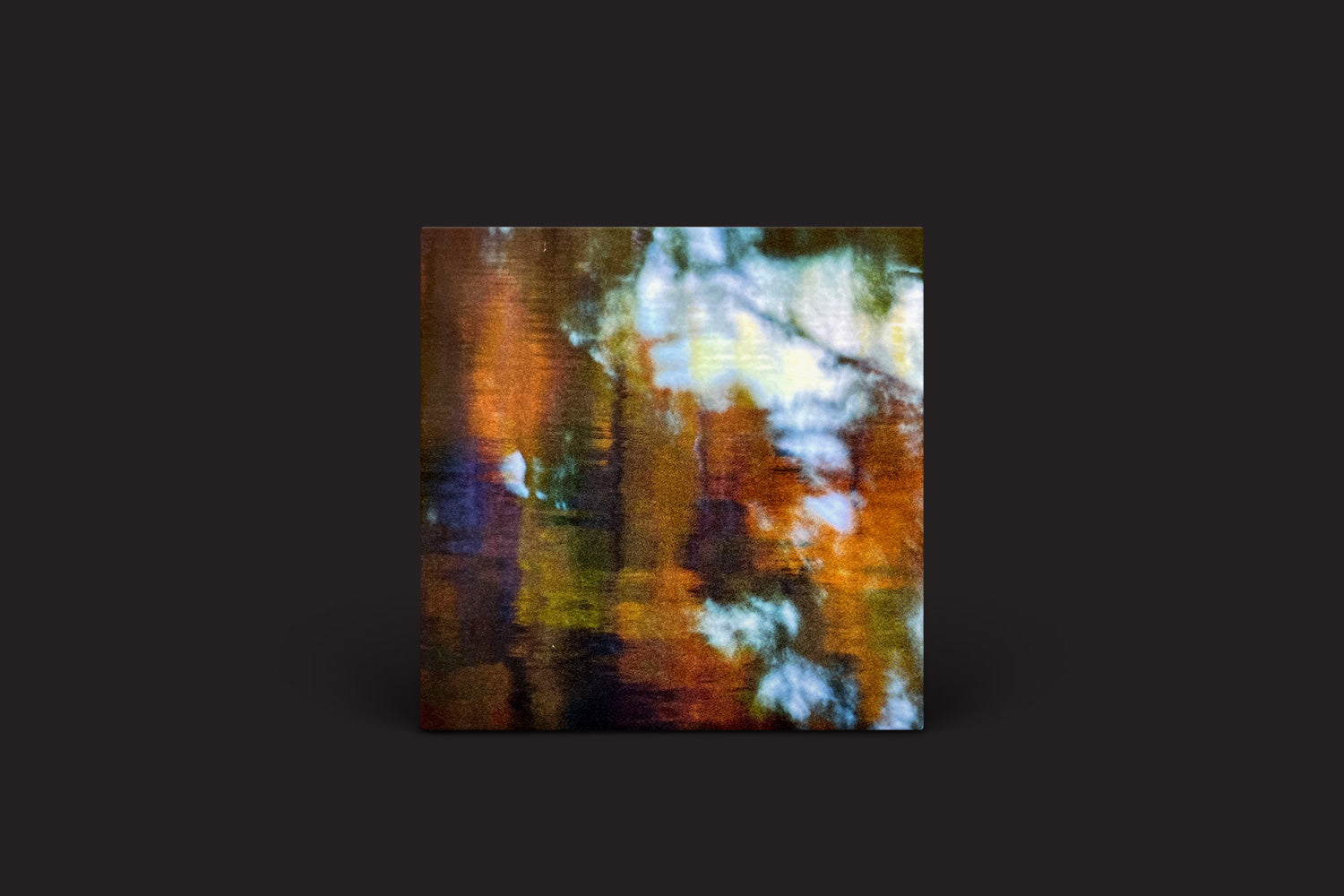 Photay com Carlos Niño: An Offering da International Anthem Recording Company apresenta uma arte abstrata que mistura cores quentes e frias — marrom, azul, laranja e verde — em harmonia improvisada. A composição desfocada acrescenta profundidade contra um fundo escuro, evocando um ambiente sonoro imaginativo.