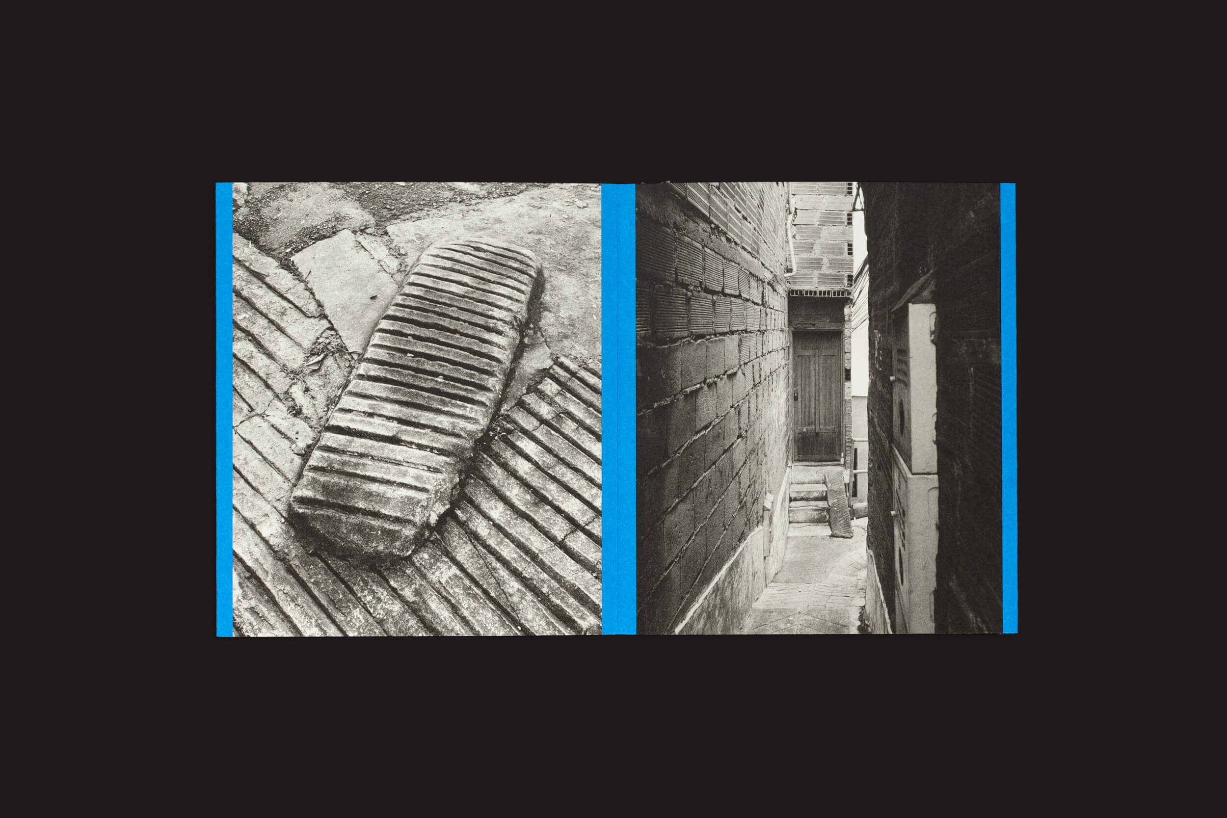 Thomas Locke Hobbs: Rampitas, de The Eriskay Connection, apresenta uma foto dividida em preto e branco encapsulando o brutalismo popular. A esquerda exibe uma pedra texturizada, enquanto a direita exibe um beco que leva a uma porta de madeira emoldurada por tijolos, artisticamente separada por bordas azuis.