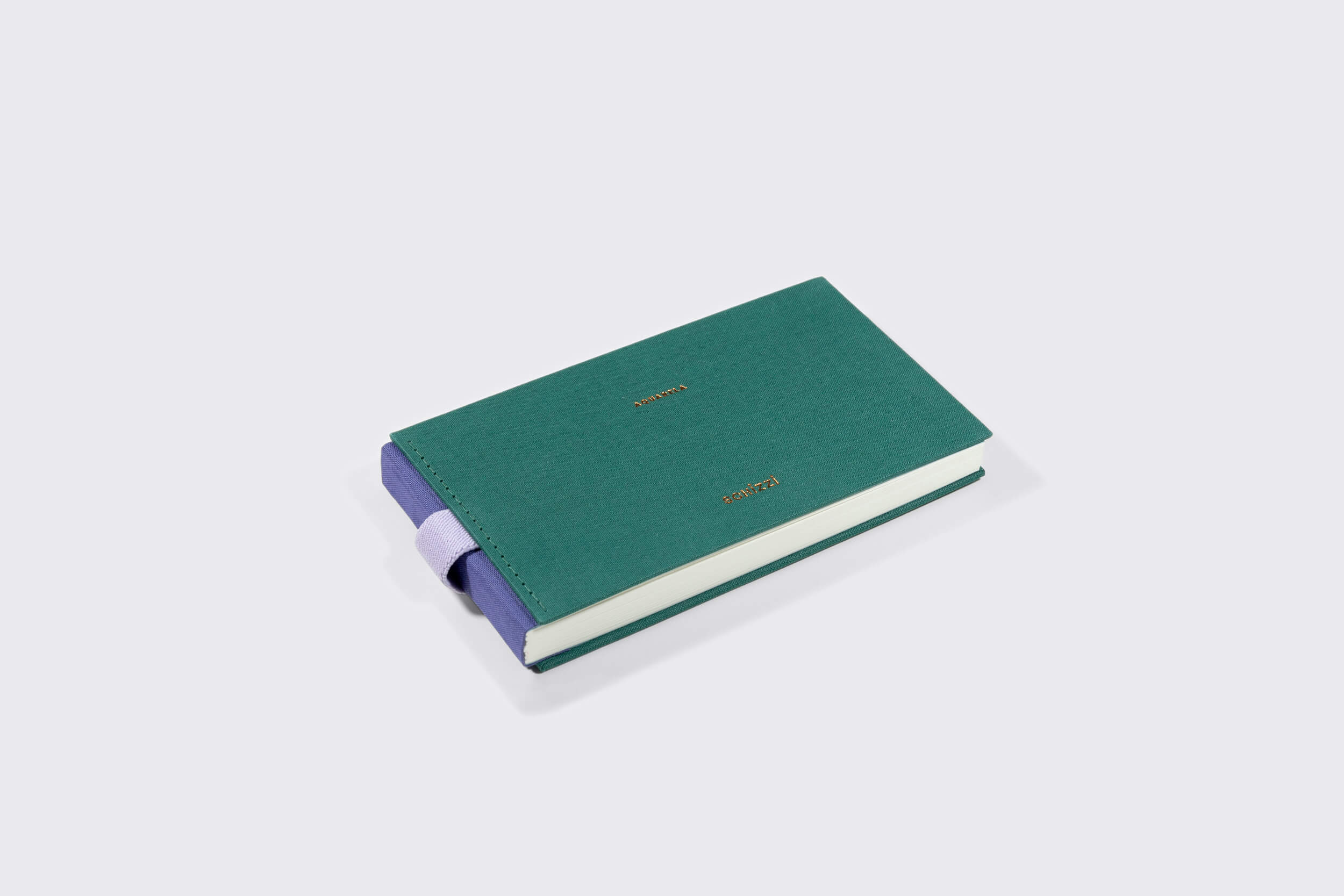 O Caderno Aquarela Pocket: Alecrim da Schizzibooks apresenta uma capa verde com texto dourado em relevo e é preso por um elástico roxo. No interior, páginas brancas aguardam seus pensamentos, descansando elegantemente em uma superfície cinza claro, prontas para serem sua tela.