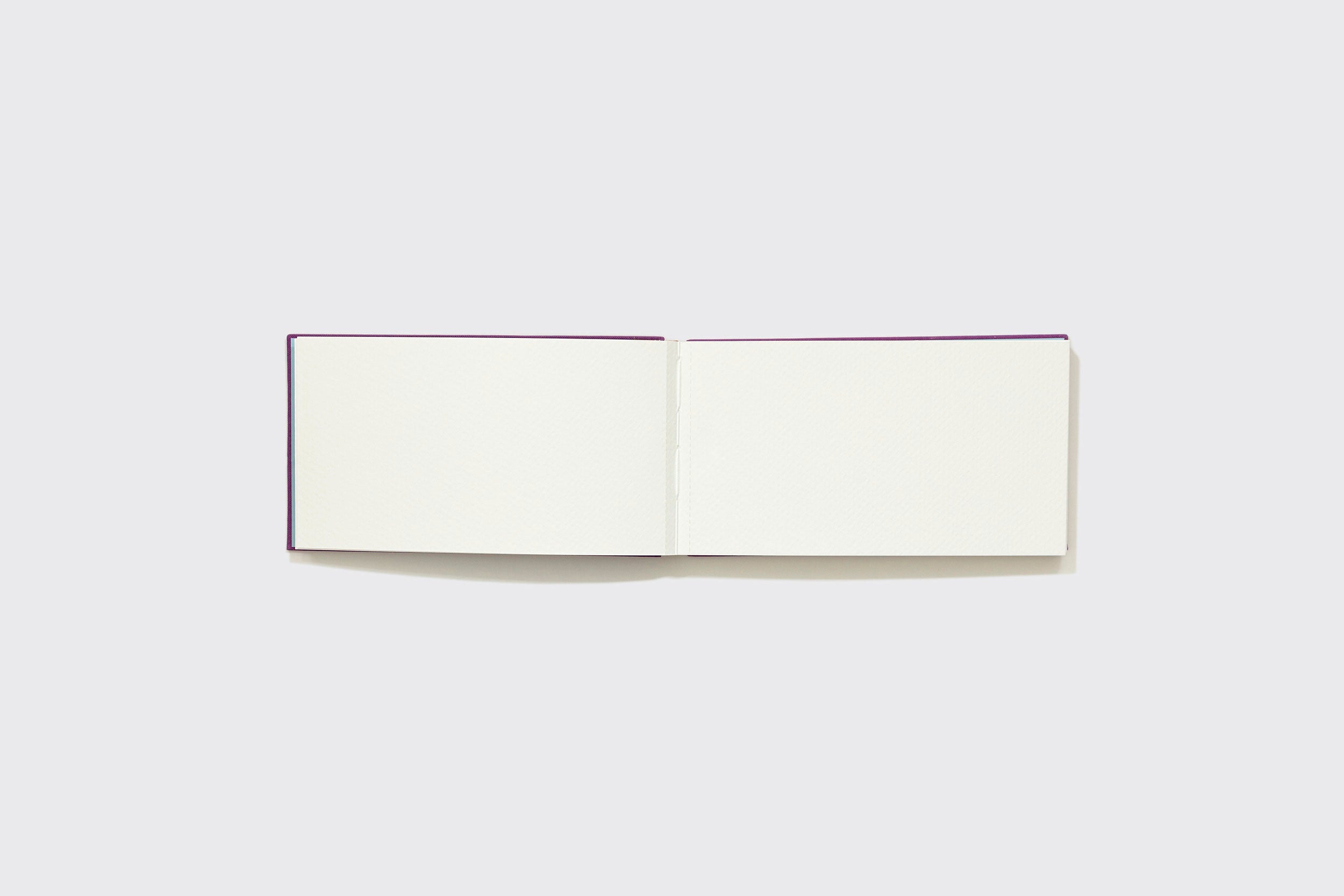 Um Caderno Aquarela Pocket da Schizzibooks com capajeira roxa está aberto sobre uma superfície cinza claro. Suas páginas de papel brancas Marcate Cottage Premium são perfeitas para seu próximo projeto criativo.