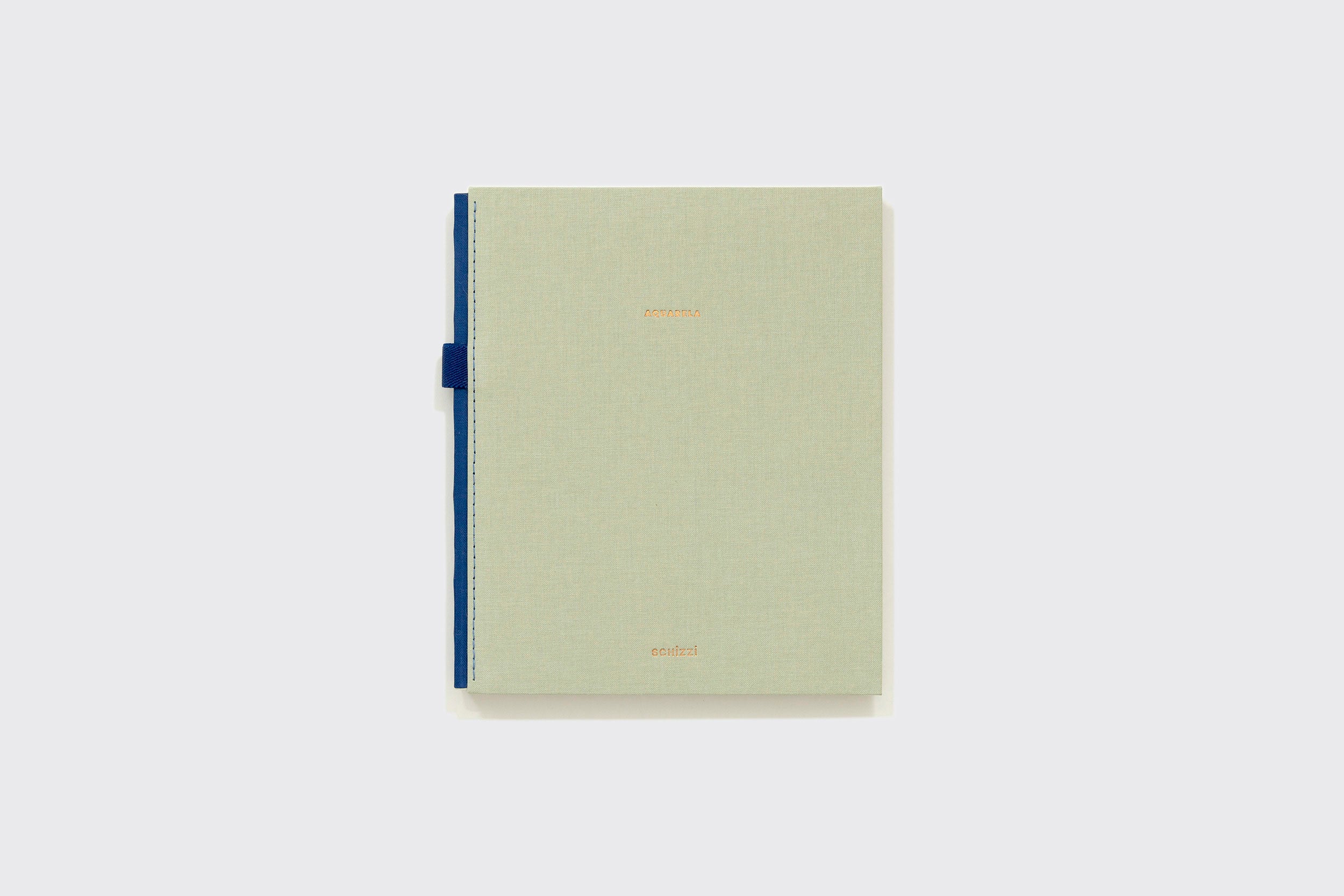 Um Caderno Aquarela verde-claro fechado da Schizzibooks com capa texturizada, texto em relevo dourado e lombada azul-escuro feito de papel Marcate Cottage Premium, sobre um fundo cinza-claro liso.