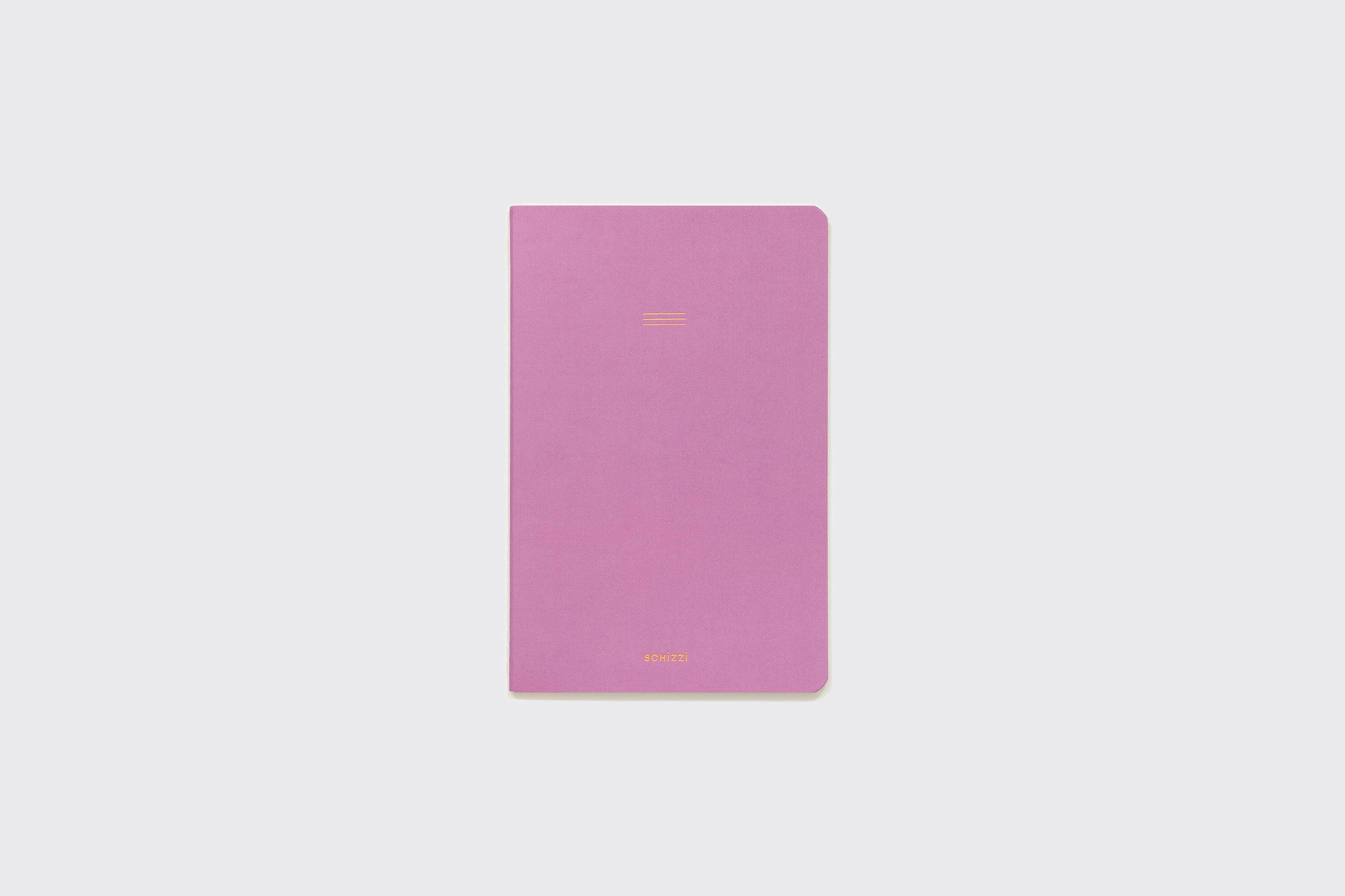 Um Caderno Flexível Schizzibooks, fechado, lilás, com cantos arredondados e texto dourado mínimo na capa frontal, centralizado sobre um fundo cinza claro.