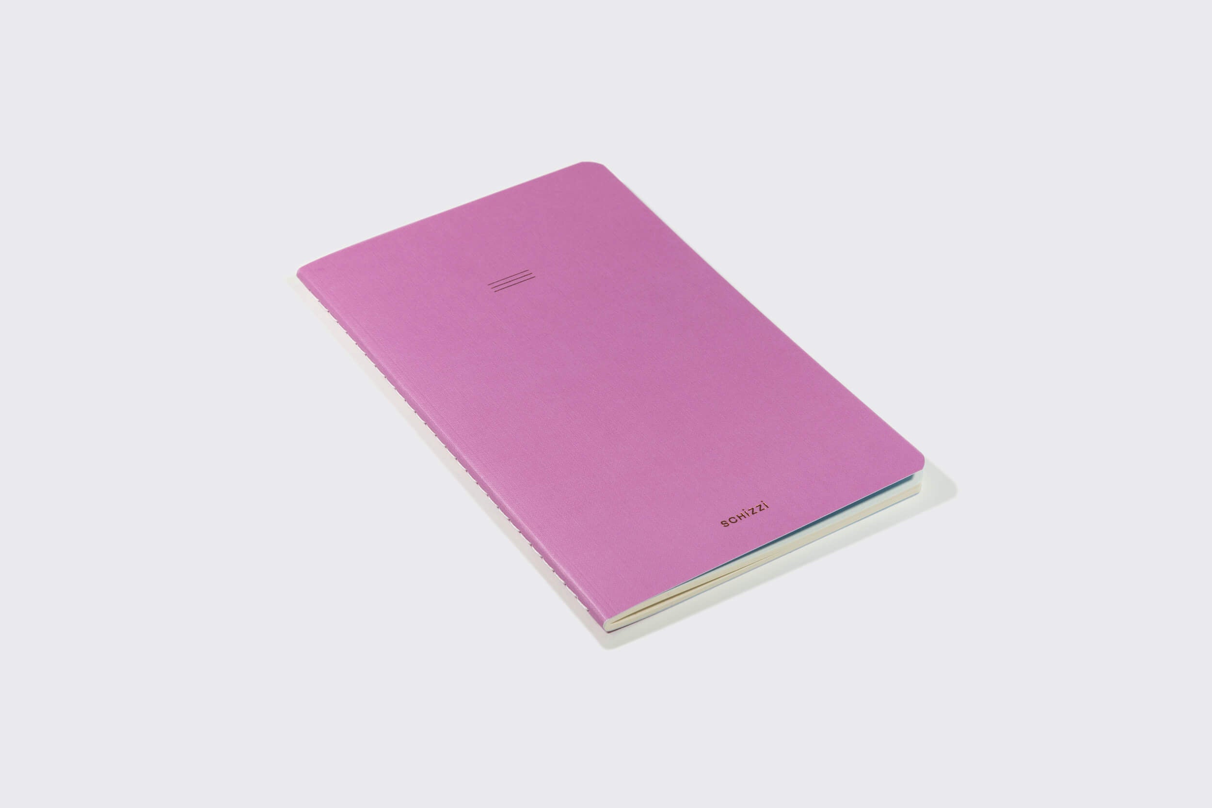 A Schizzibooks Caderno Flexível: Mirtilo, com um design de capa rosa minimalista, repousa sobre uma superfície branca. Sua leve sombra direita sugere sua qualidade artesanal.