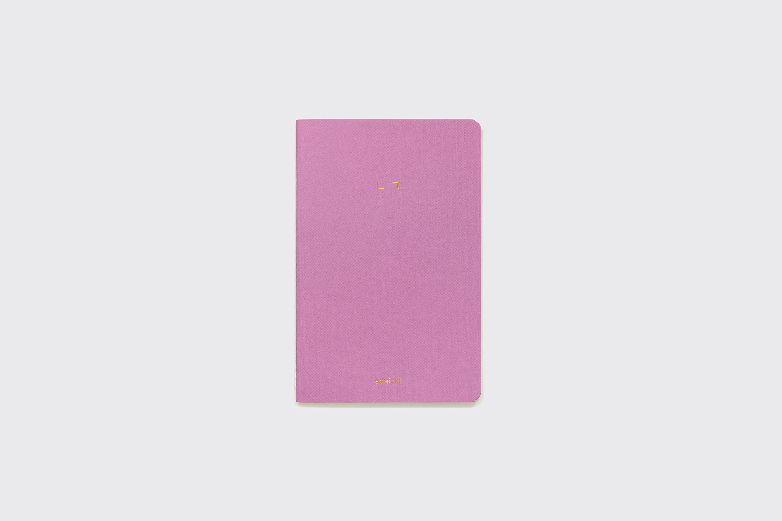 Um Caderno Flexível roxo, fechado, da Schizzibooks, com cantos arredondados, está centralizado sobre um fundo cinza claro liso. A capa do caderno apresenta um texto dourado minimalista próximo à parte superior e inferior.