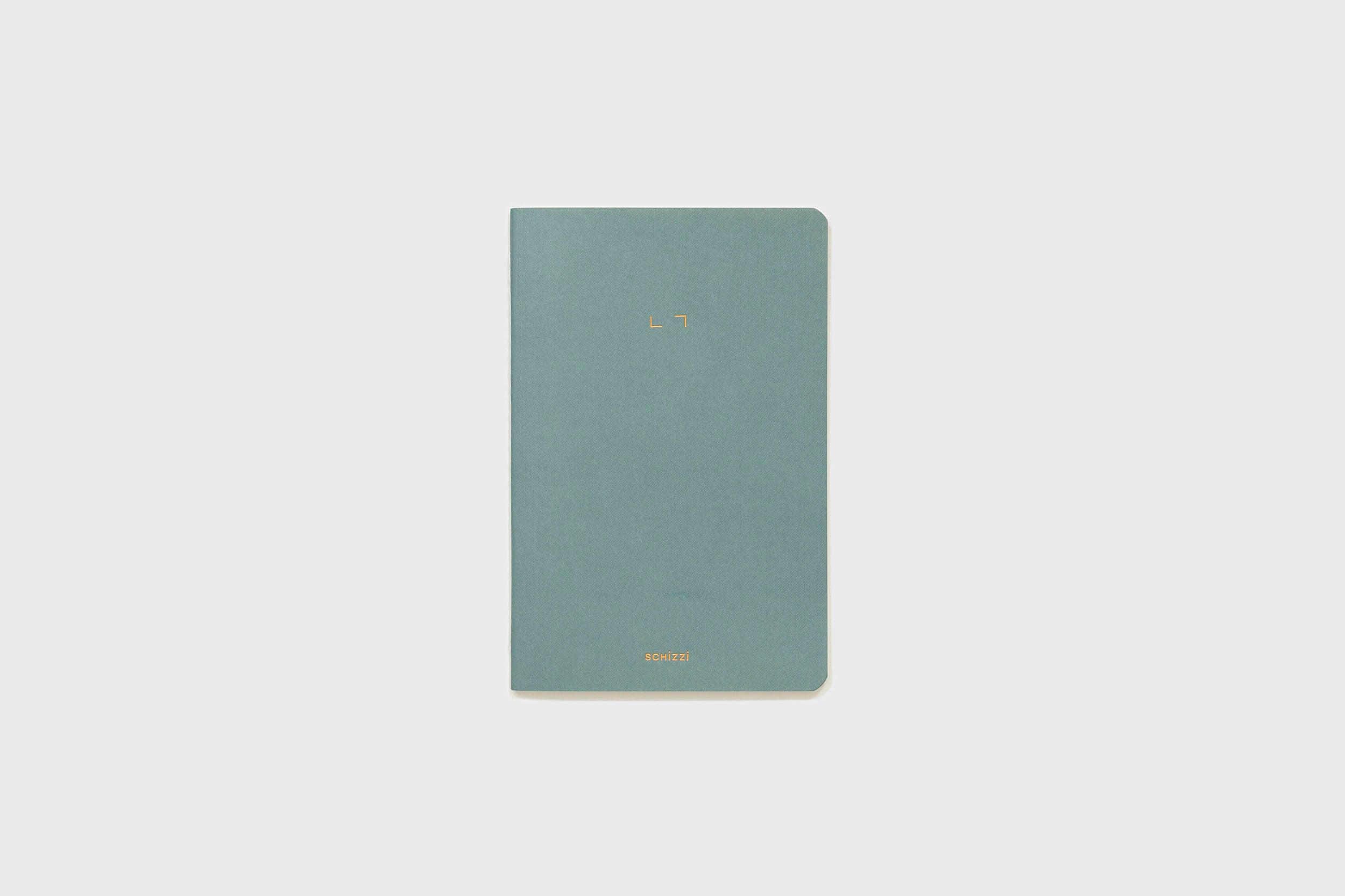 Um Caderno Flexível fino e fechado da Schizzibooks, na cor azul-petróleo com cantos arredondados e texto dourado mínimo, produzido manualmente no Brasil, está sobre um fundo cinza claro simples.