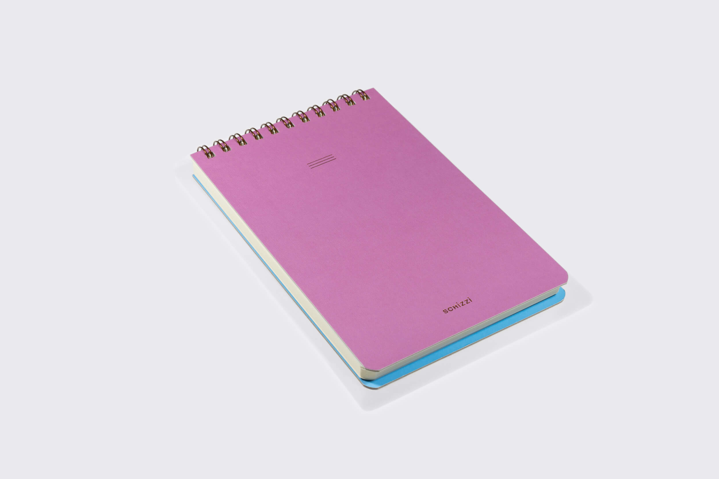 Um Caderno Reporter: Mirtilo da Schizzibooks encadernado em espiral com capa rosa repousa sobre uma superfície branca, com páginas de bordas azuis feitas de papel pólen macio. Este caderno tem um design simples e minimalista e reflete a produção manual no Brasil.