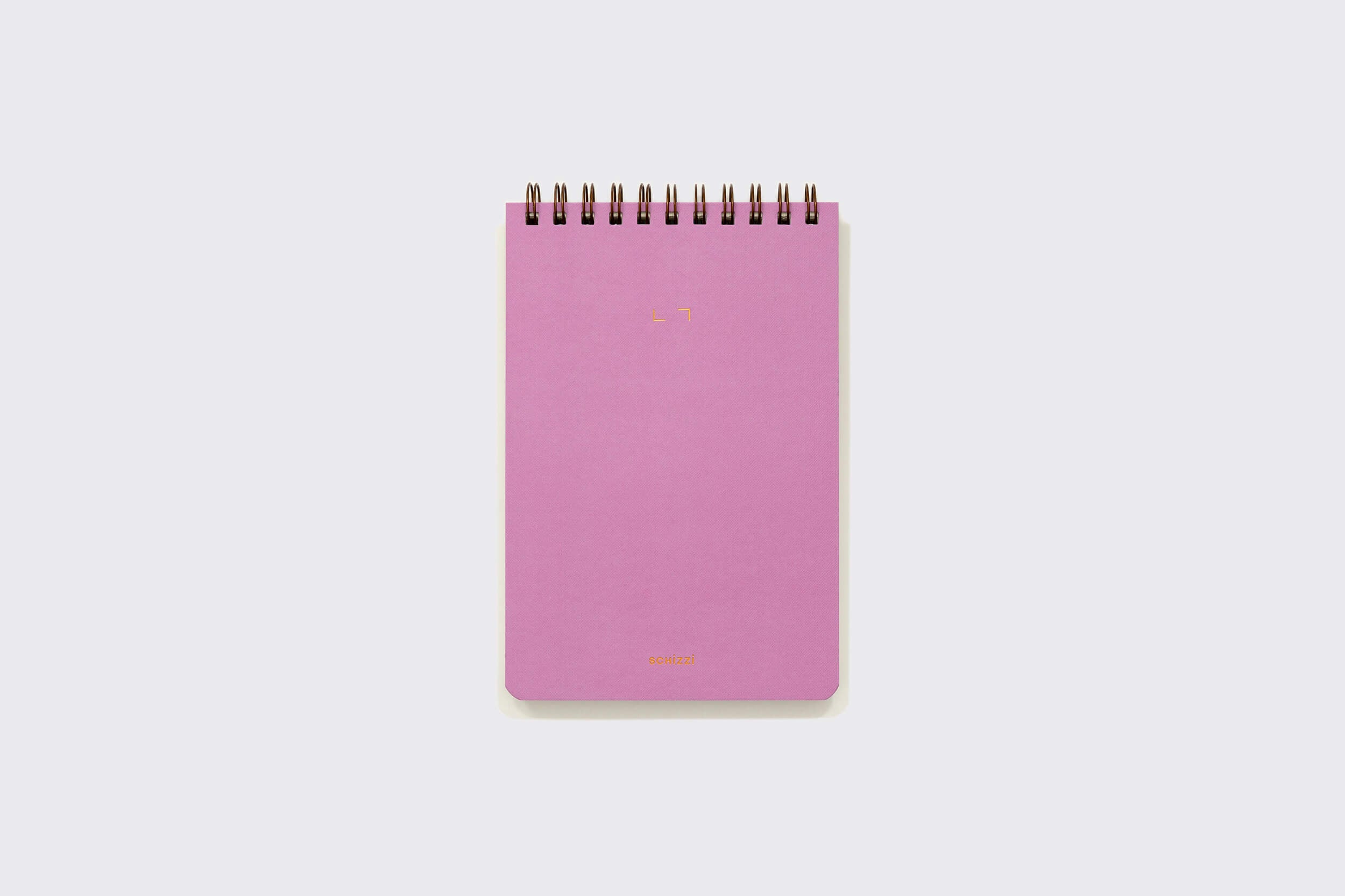 Um Caderno Reporter: Mirtilo da Schizzibooks, rosa, encadernado em espiral, com design minimalista, repousa sobre uma superfície cinza claro, com texto discreto nas partes superior e inferior central de sua capa mole de papel pólen — uma prova do artesanato especializado e da produção manual no Brasil.