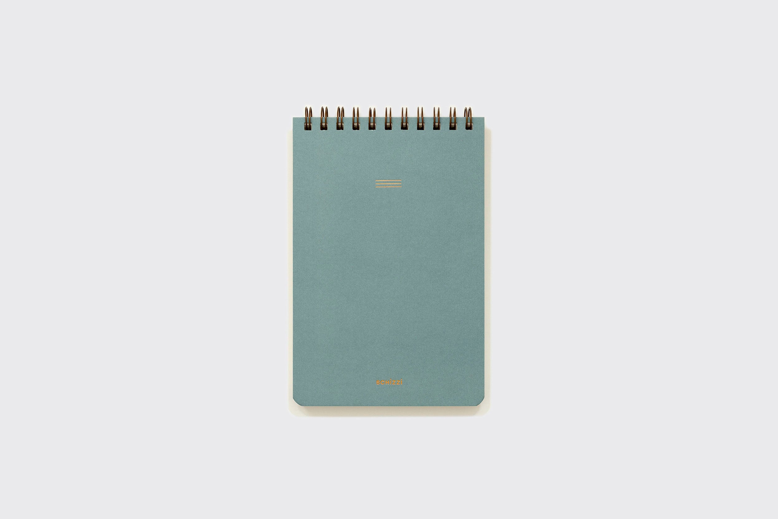 Um pequeno caderno espiral azul da Schizzibooks Caderno Reporter, com capa lisa e texto dourado, feito à mão com papel sem ácido, centralizado em um fundo cinza claro.