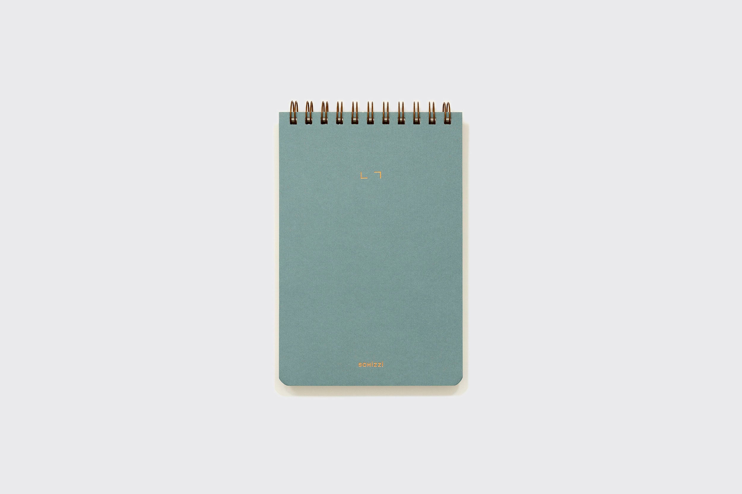 Um Caderno Reporter da Schizzibooks, encadernado em espiral azul-esverdeado, com design minimalista e texto de capa dourado, feito à mão em papel sem ácido, é colocado verticalmente sobre um fundo cinza claro.