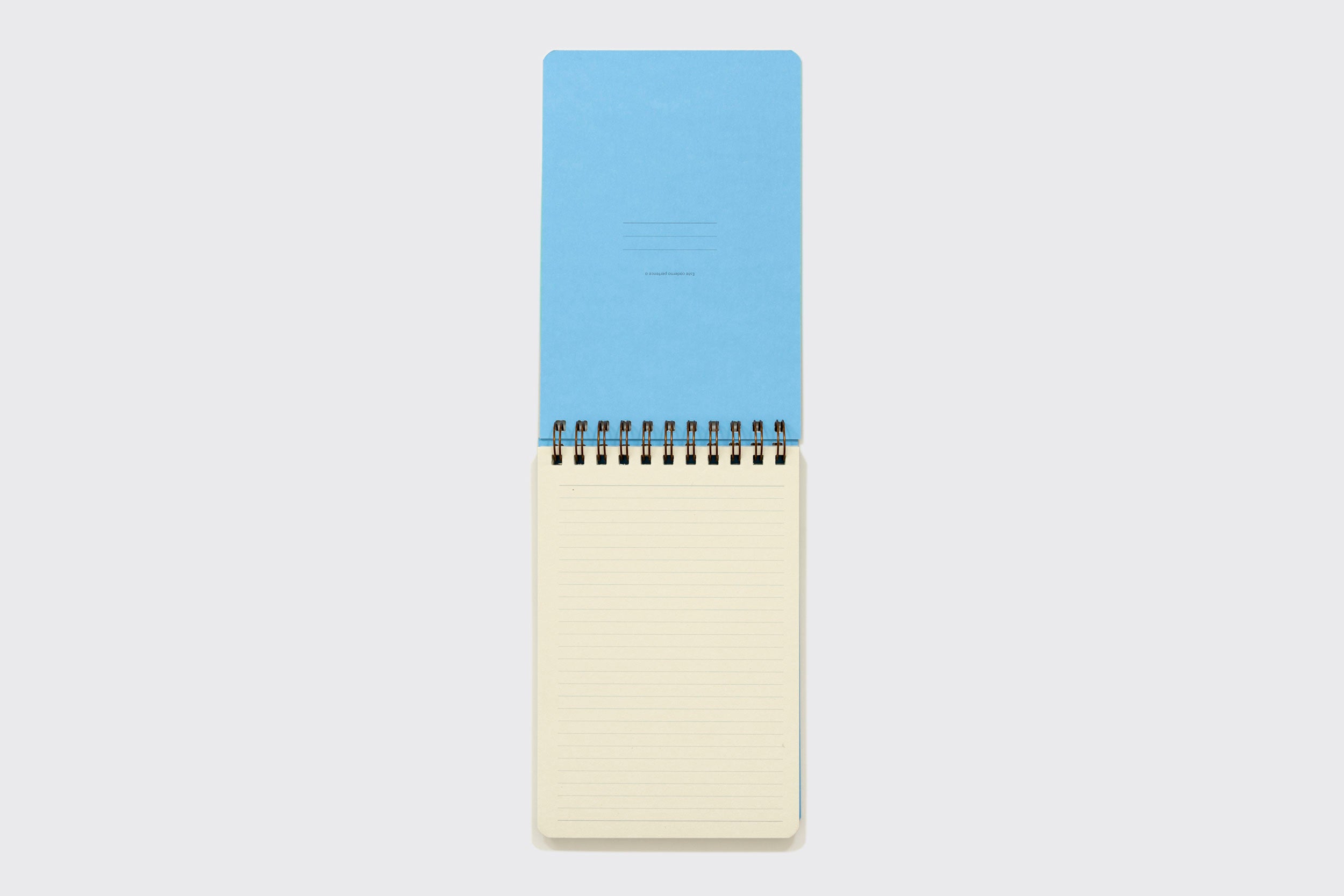 Um caderno espiral Caderno Reporter da Schizzibooks com capa azul está aberto em uma página bege pautada em branco, de papel sem ácido, sobre um fundo branco liso.