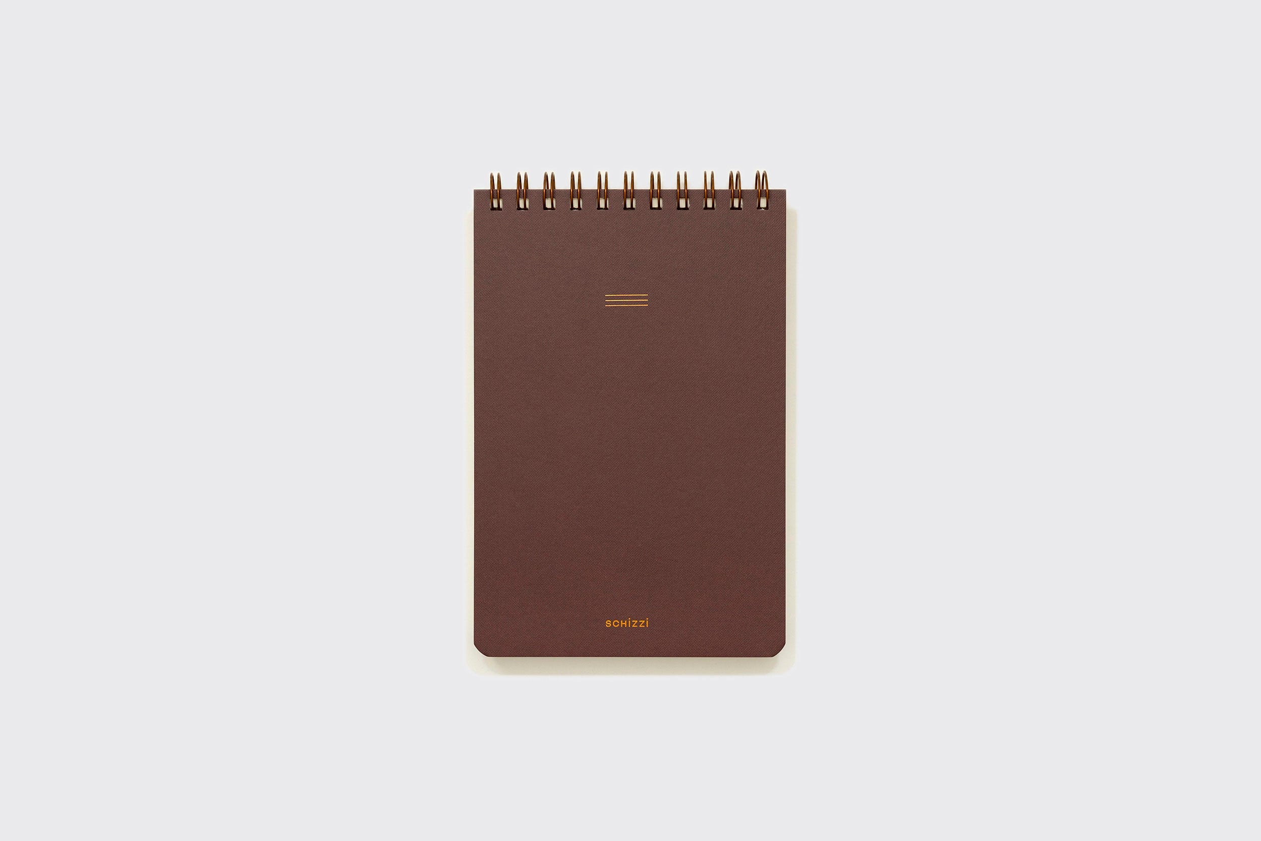 Um bloco de notas médio Caderno Reporter da Schizzibooks marrom com cantos arredondados, linhas minimalistas douradas, "setizi" na parte inferior e papel sem ácido para maior durabilidade está centralizado em um fundo cinza claro.