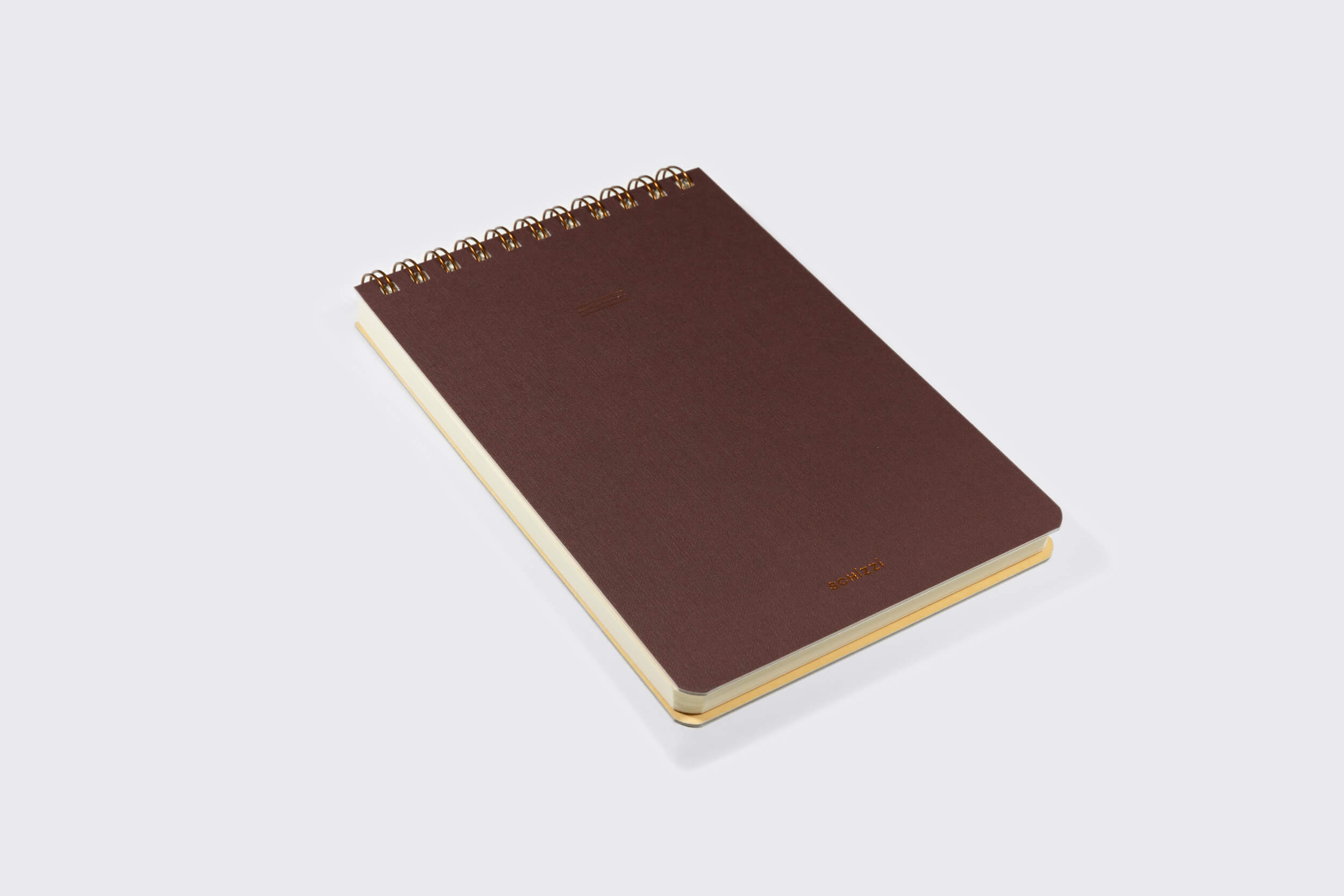 Um Caderno Reporter fechado: Savana da Schizzibooks fica em uma superfície branca. O visual minimalista deste caderno espiral marrom não tem marcas, com páginas creme claras feitas manualmente usando papel livre de ácidos para maior durabilidade.