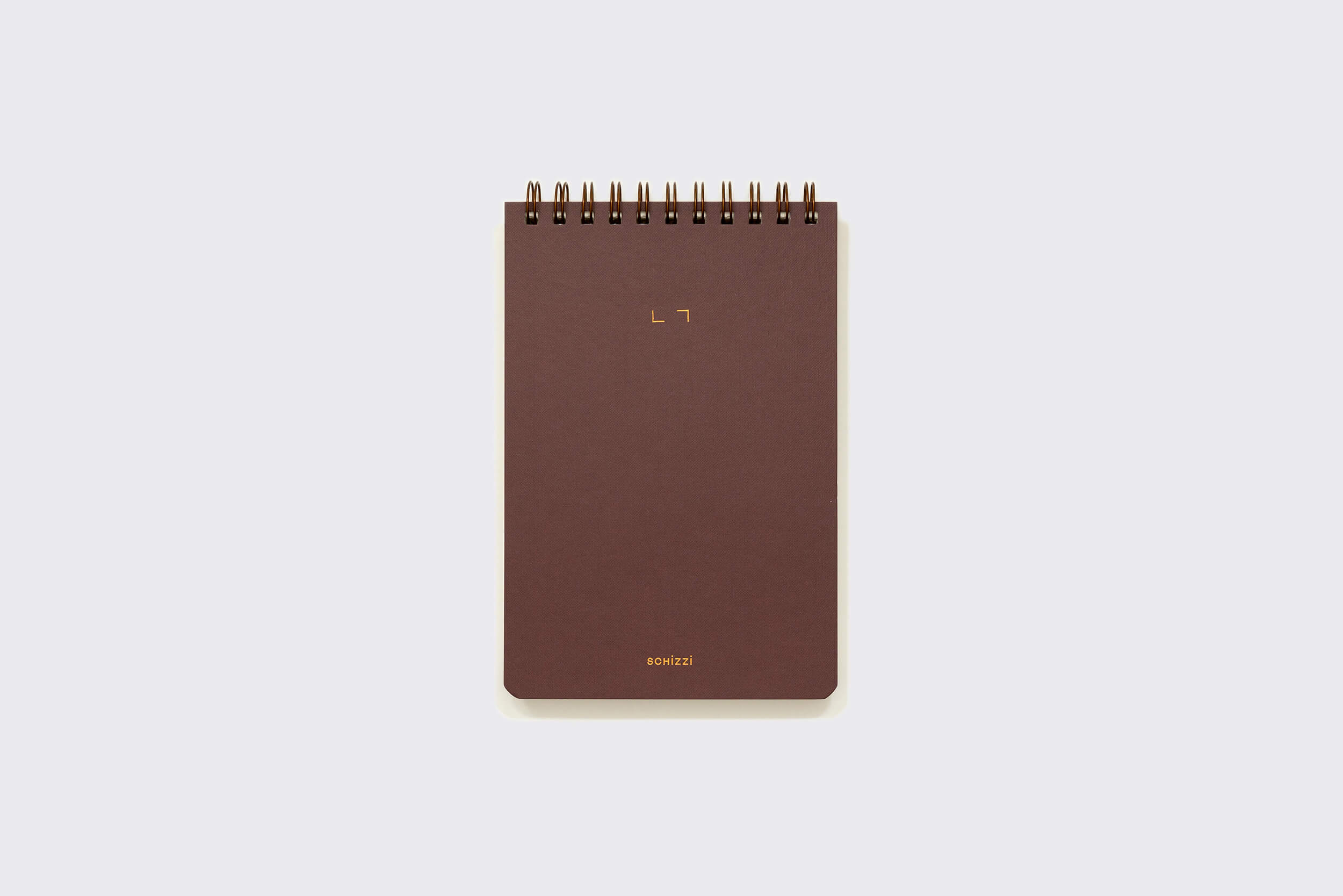 O Caderno Reporter: Savana da Schizzibooks é um bloco de notas marrom, encadernado em espiral, com um design minimalista em um fundo cinza. Sua capa exibe um pequeno texto dourado perto do topo e da base. Este bloco feito à mão é papel livre de ácidos, garantindo que suas notas sejam preservadas lindamente.